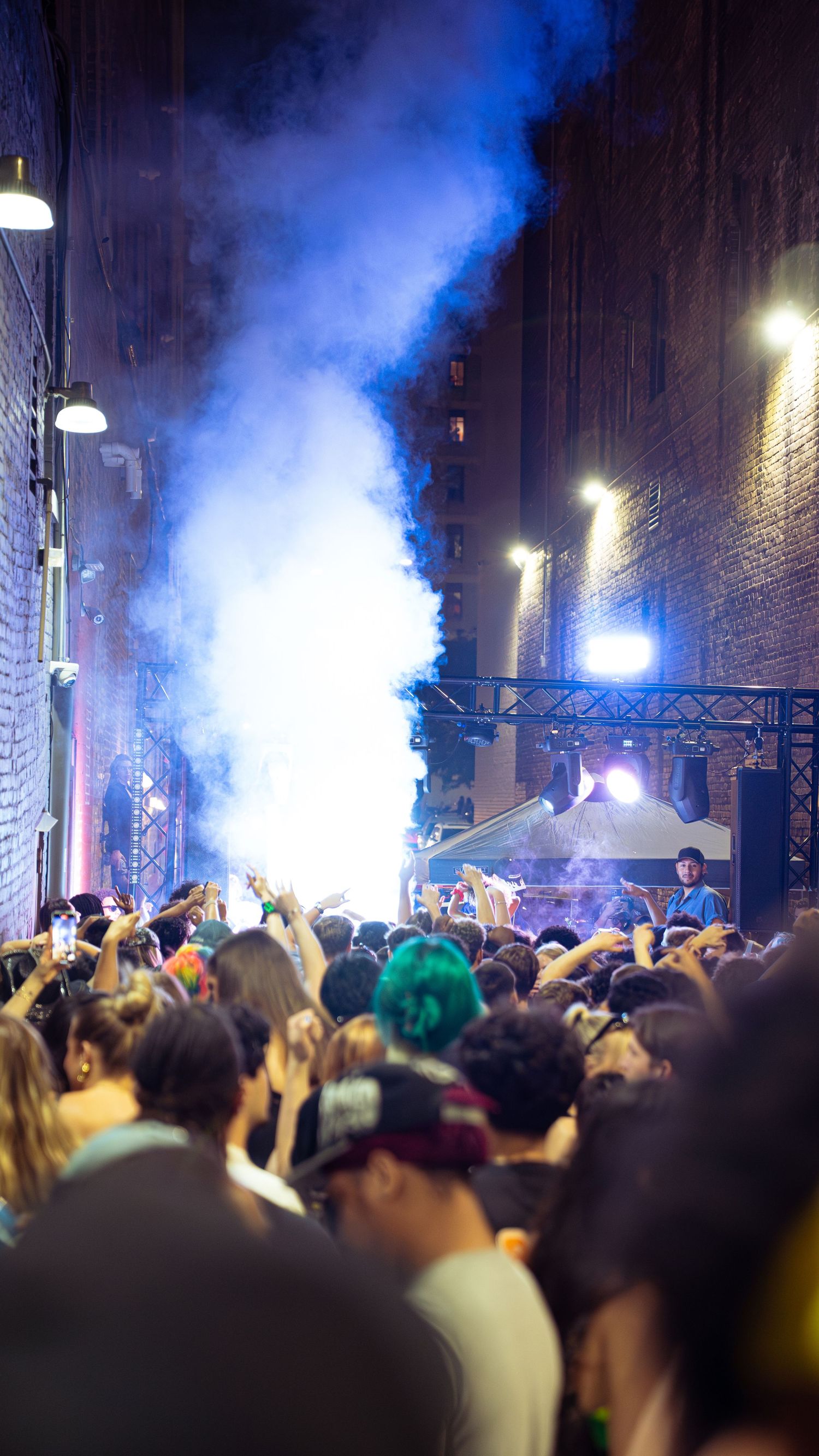 Blue smoke effect illuminates crowd at outdoor nighttime event.