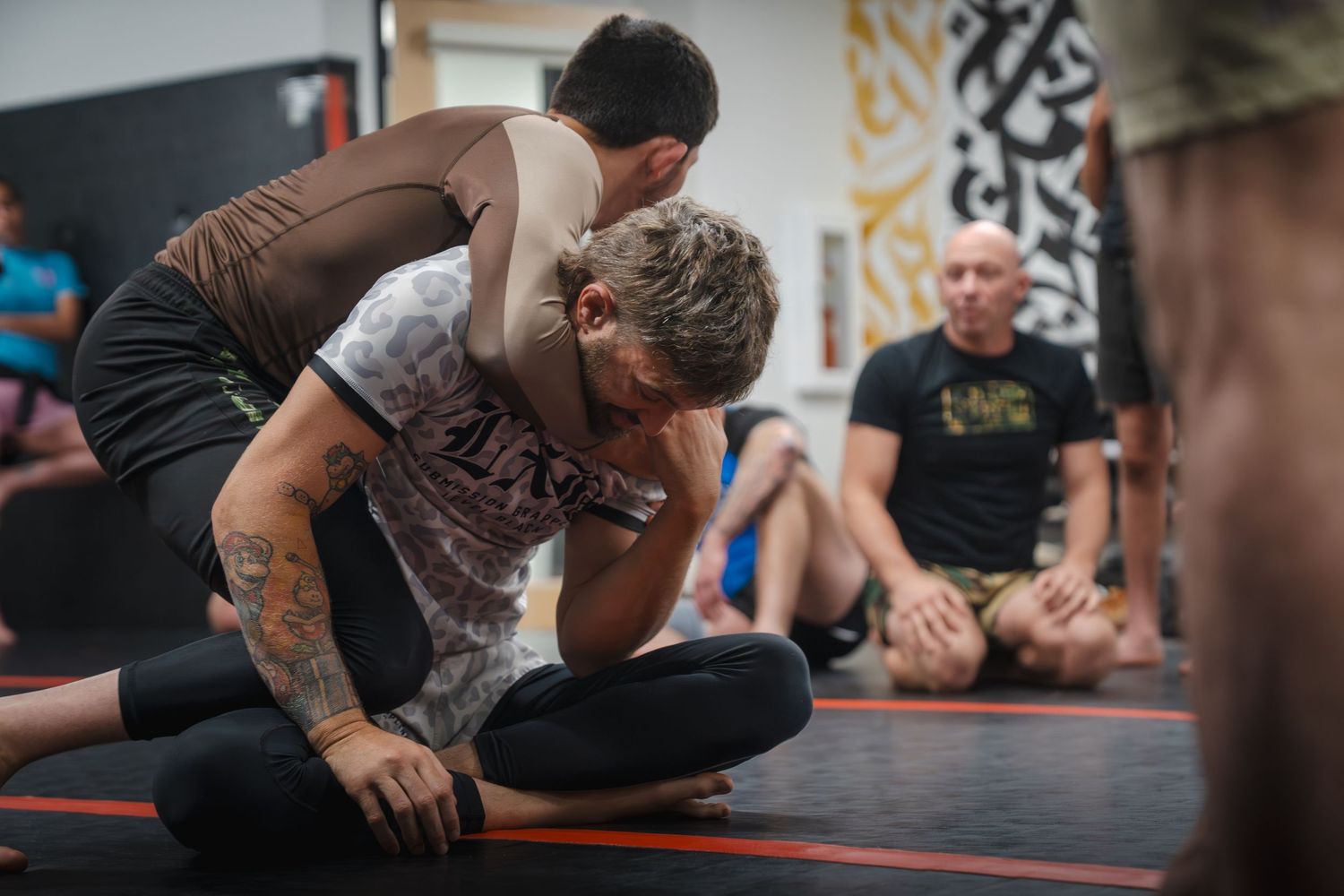 Two athletes demonstrating grappling techniques on training mats during practice.