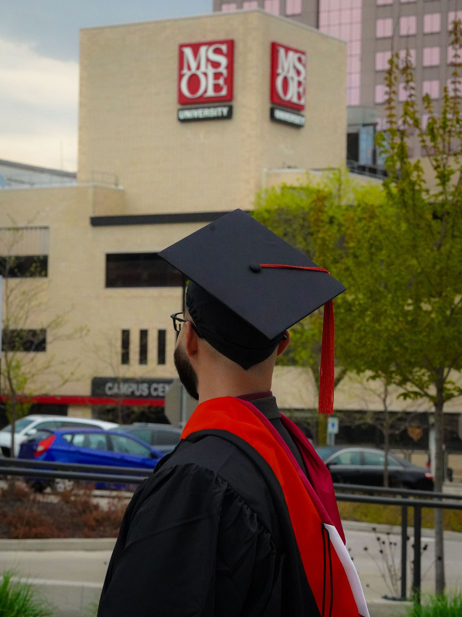 Graduate stands near MSOE University building with graduation cap and gown during commencement ceremony.