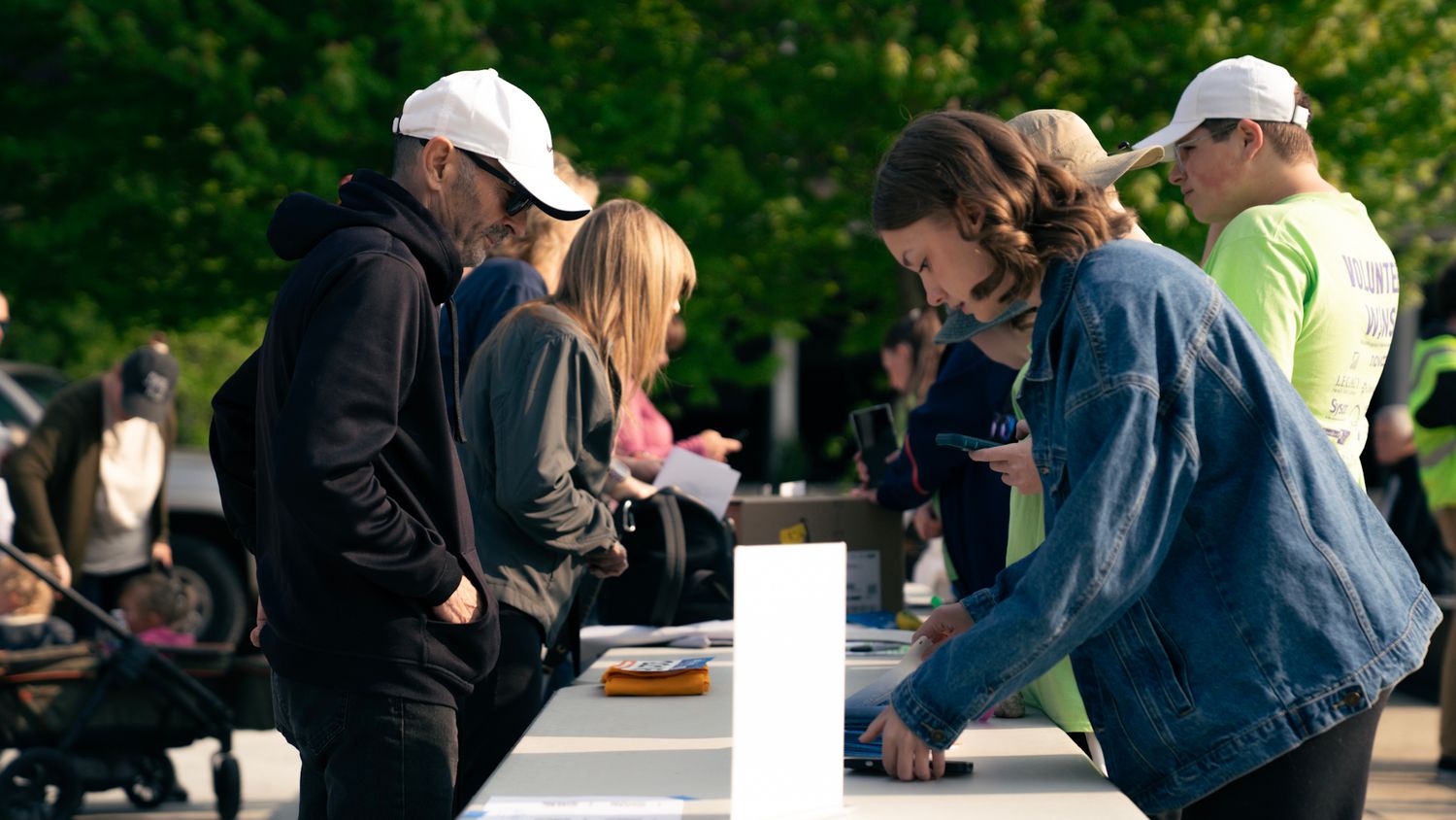 A group of people gather around a white table at an outdoor event checking in or registering.
