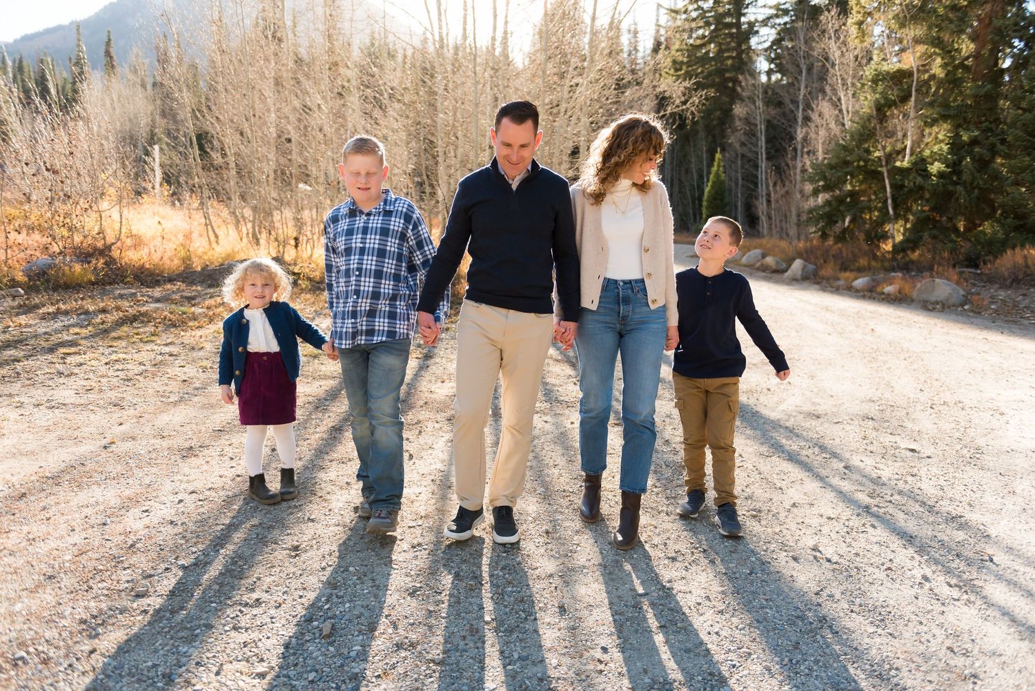 Group walks together holding hands on a dirt mountain road during golden hour casting long shadows.