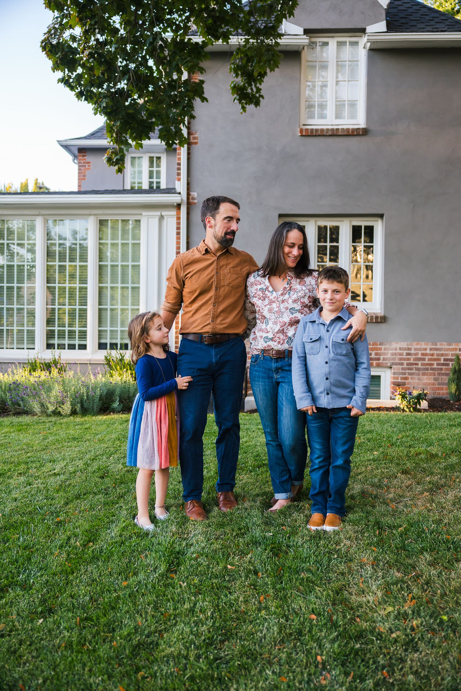 A family poses together on their lawn in front of a gray house with large windows.