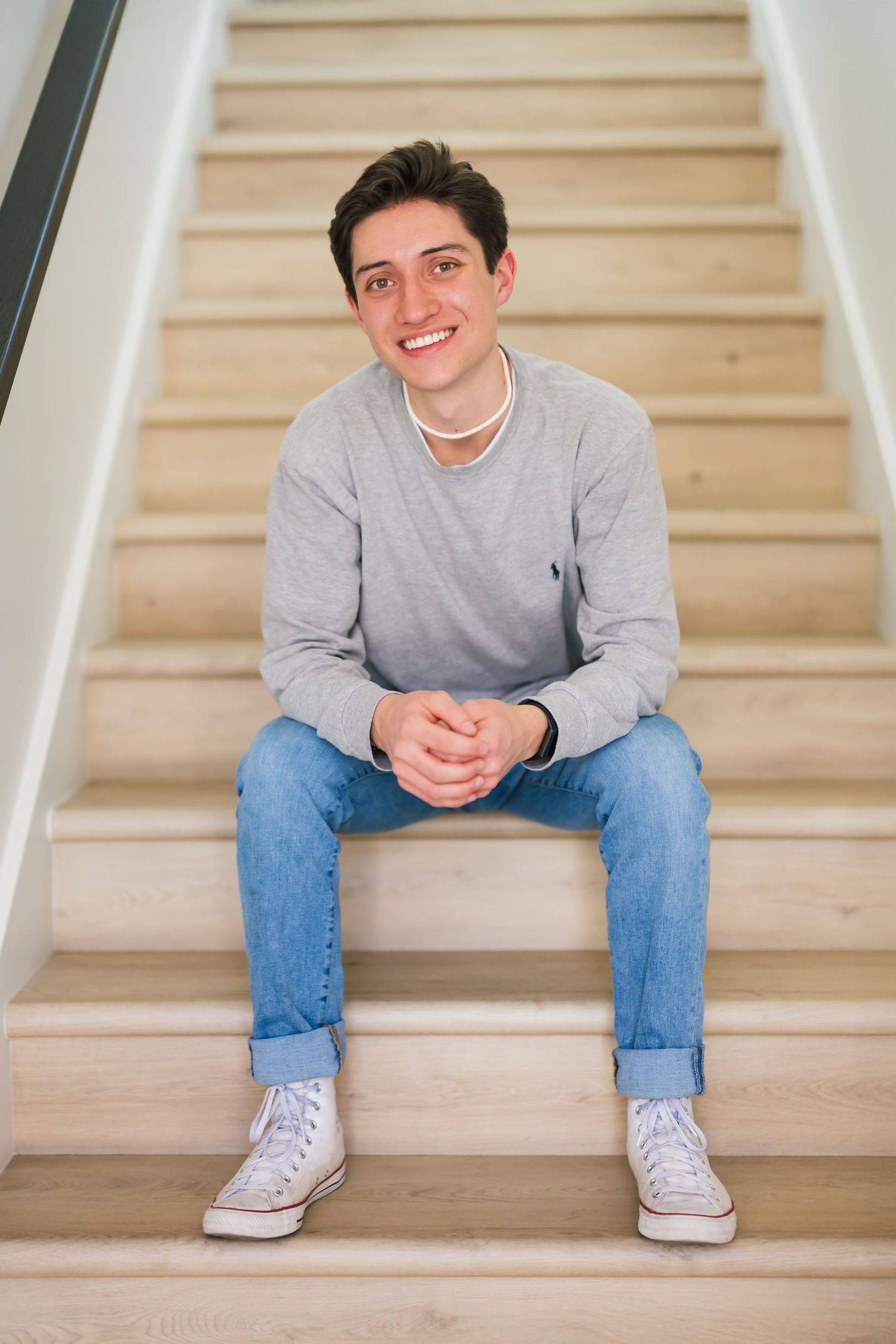 senior in grey sweatshirt and jeans sitting on wooden stairs in casual poses at utah studio