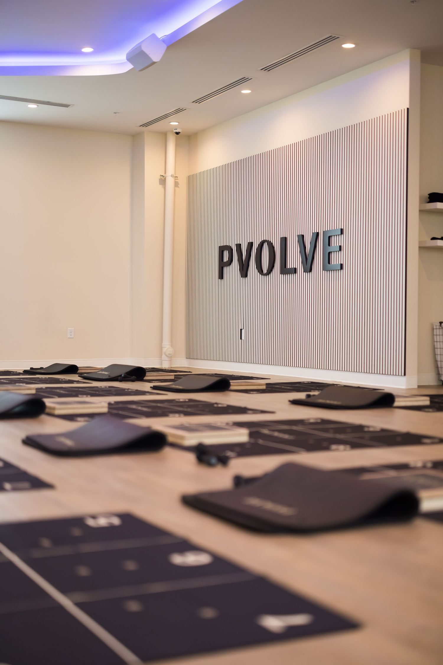 Interior of a Pvolve fitness studio showing wall logo and exercise mats laid out on the floor with blue ambient lighting.