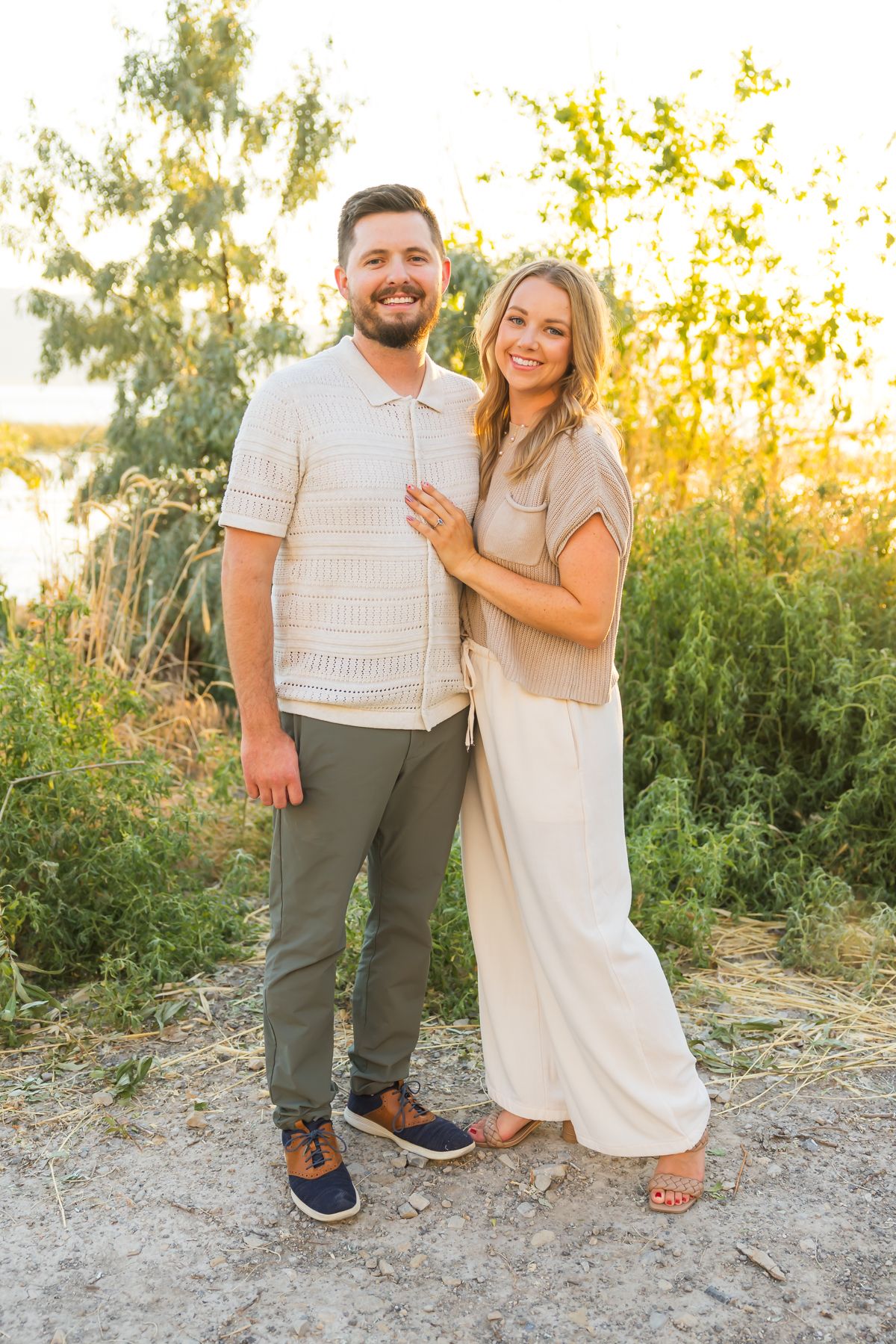 Happy couple in coordinated neutral outfits poses together against sunset-lit natural backdrop.
