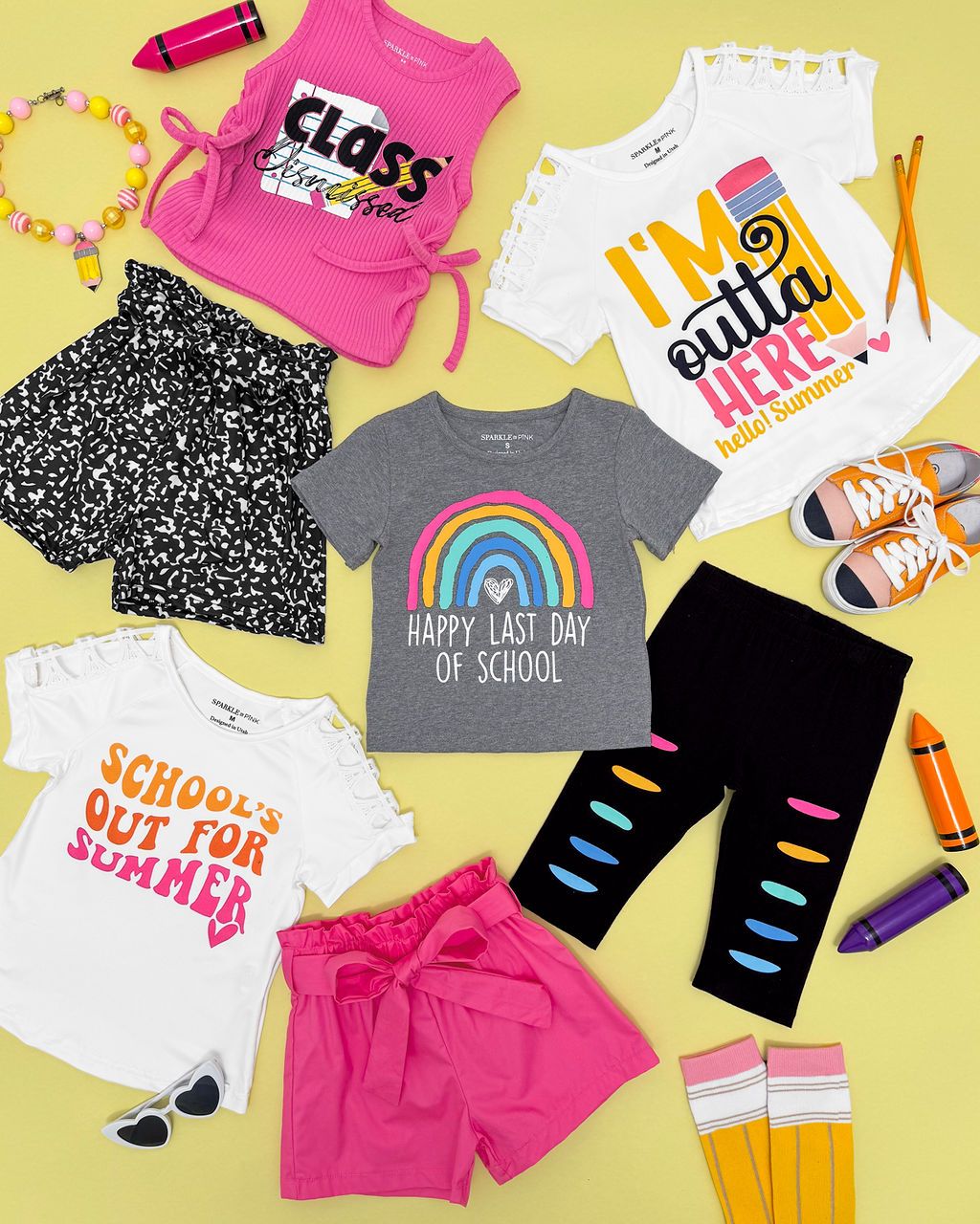 Colorful back to school clothing collection featuring rainbow prints, pink shorts, and graphic t-shirts laid out on yellow background.