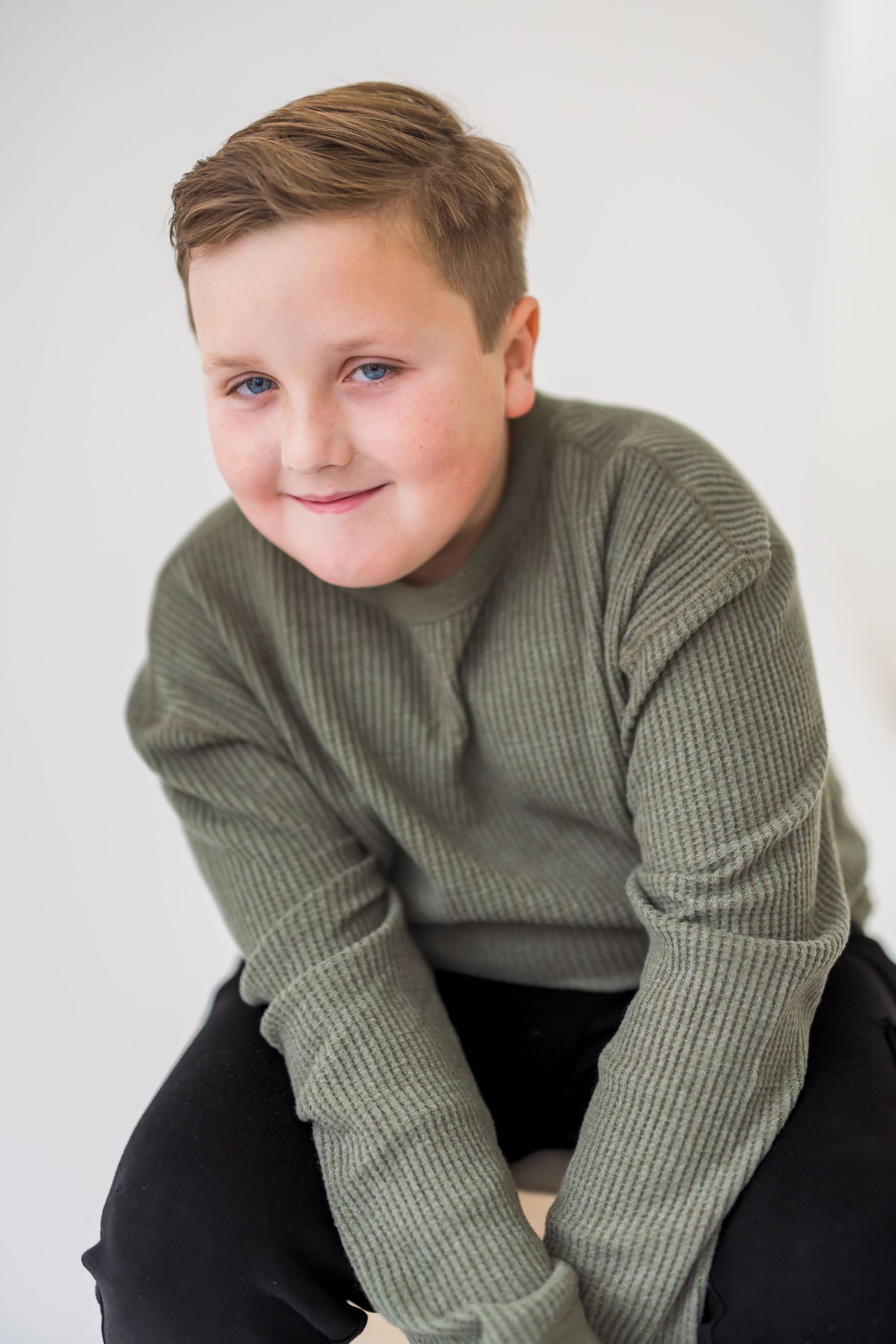 A young person wearing a green ribbed sweater poses against a white background in a series of candid shots.