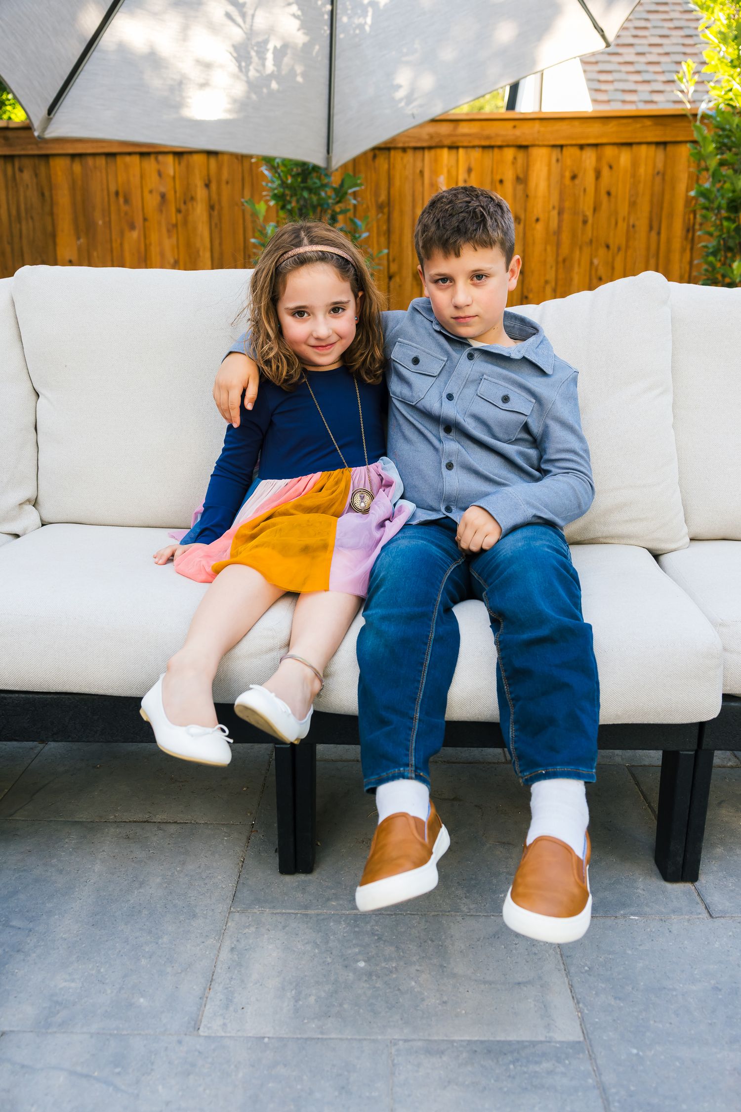 Two children posing together on white outdoor sofa.