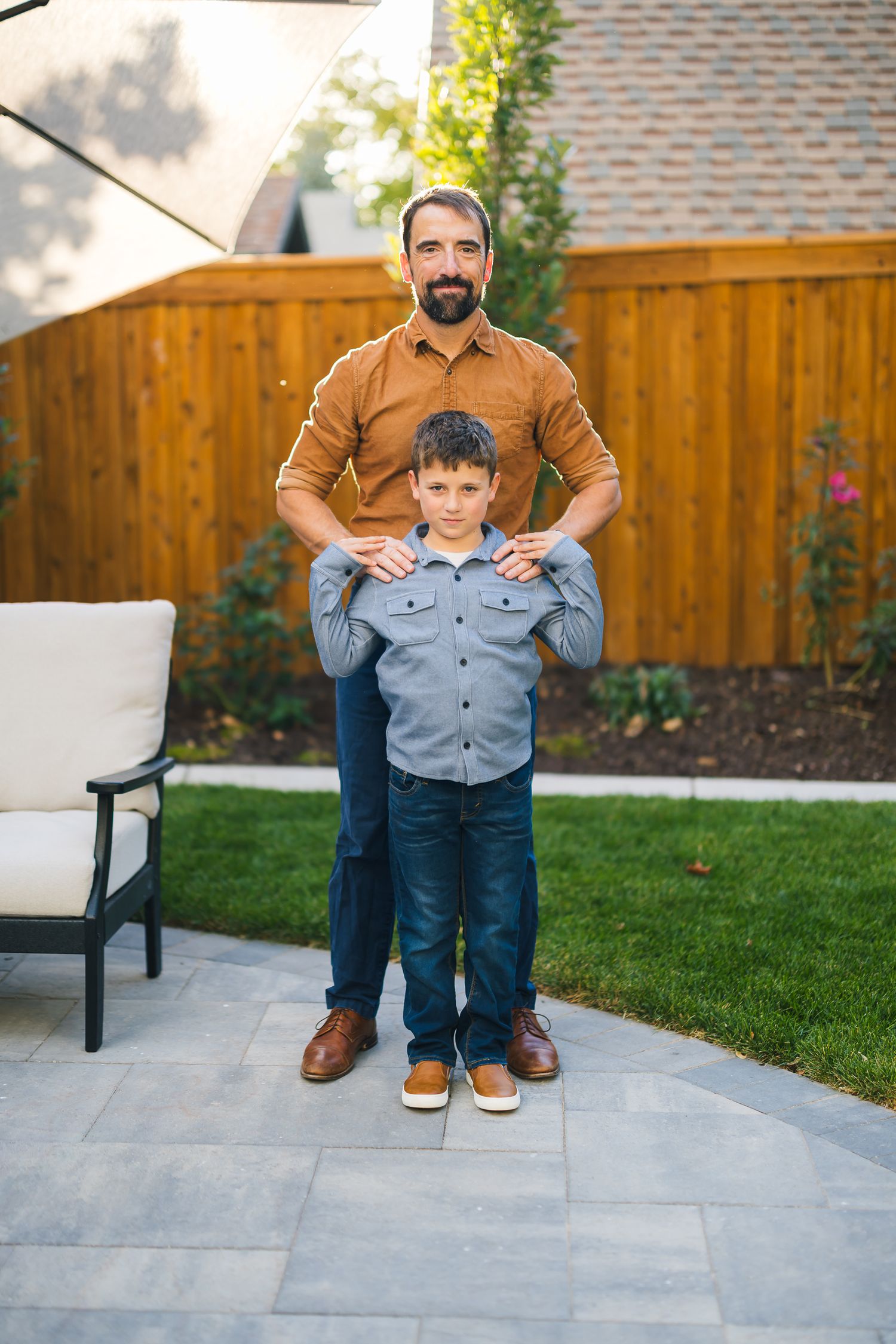 Parent and child standing together on stone patio with wooden fence in background.