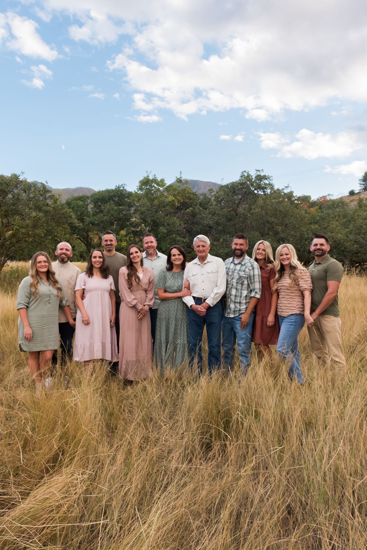 Large group gathered in golden field for casual outdoor photoshoot with mountains in background.