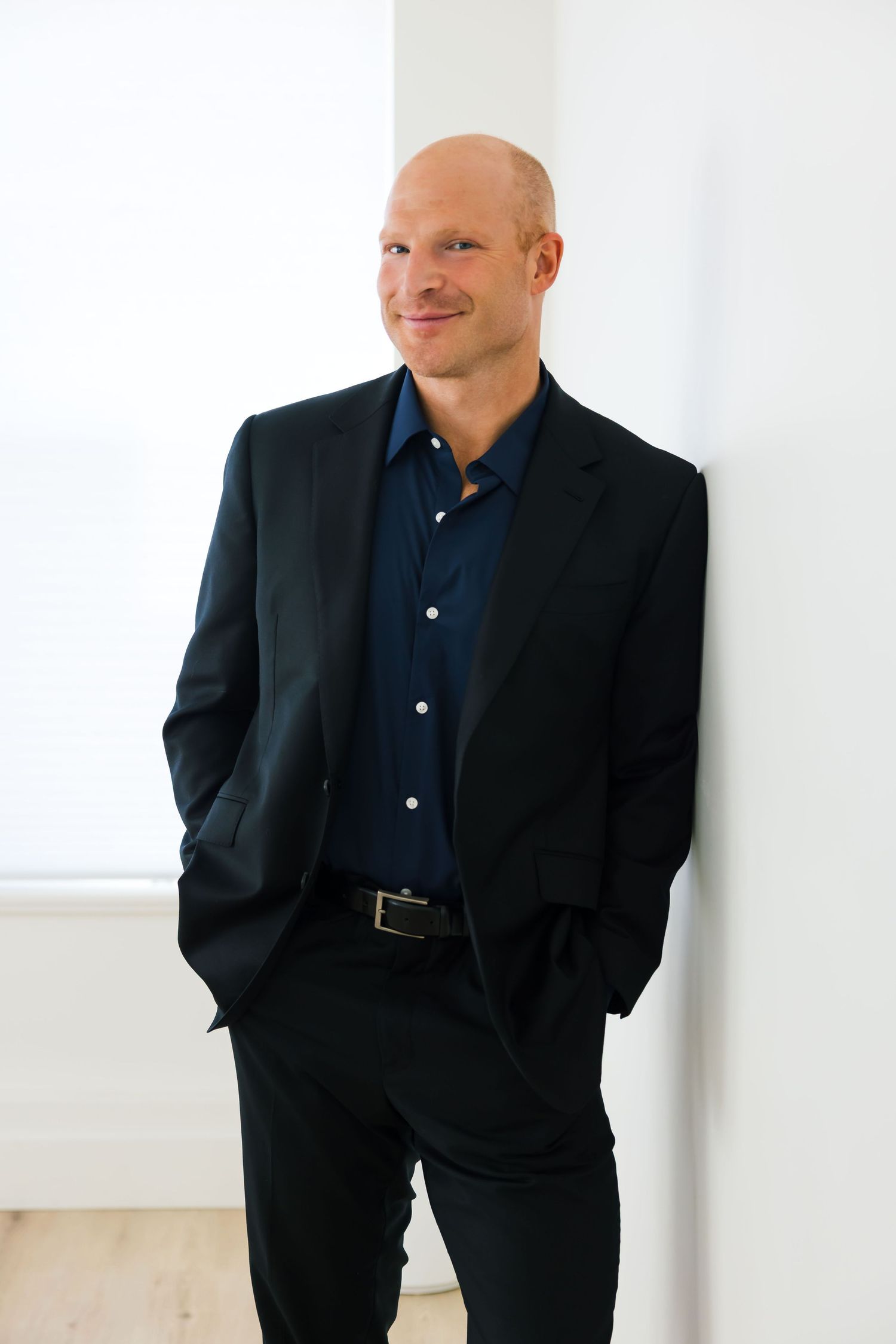 Professional business portrait showing person in dark suit and navy shirt against white background.