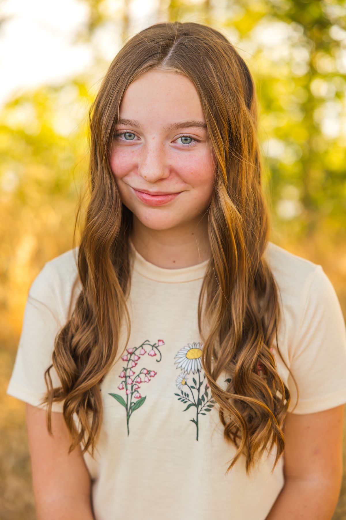 Portrait of a person wearing a floral t-shirt with long wavy hair in golden sunset lighting.