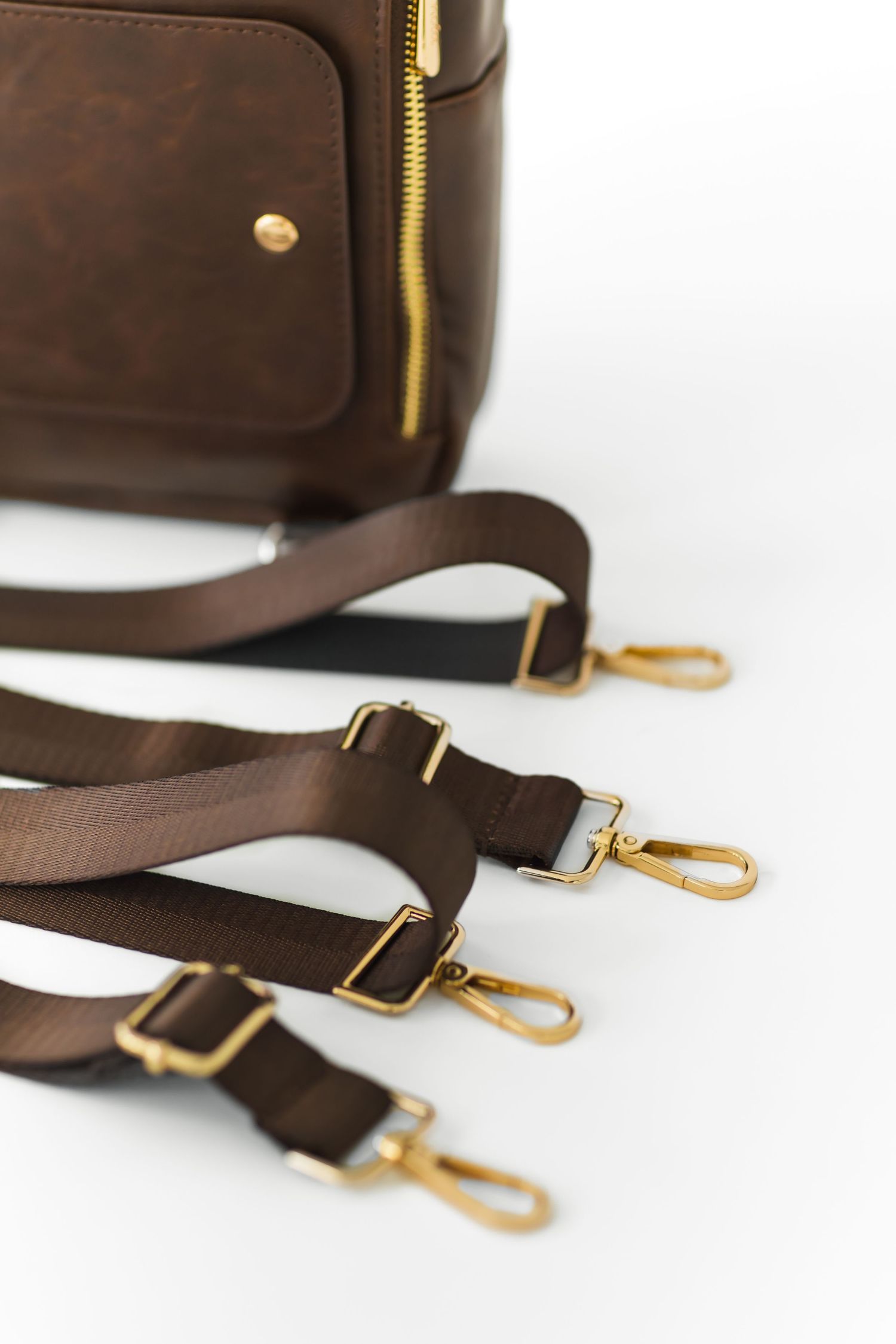 Brown leather bag straps with brass hardware and clips arranged on white background showing adjustable length details.