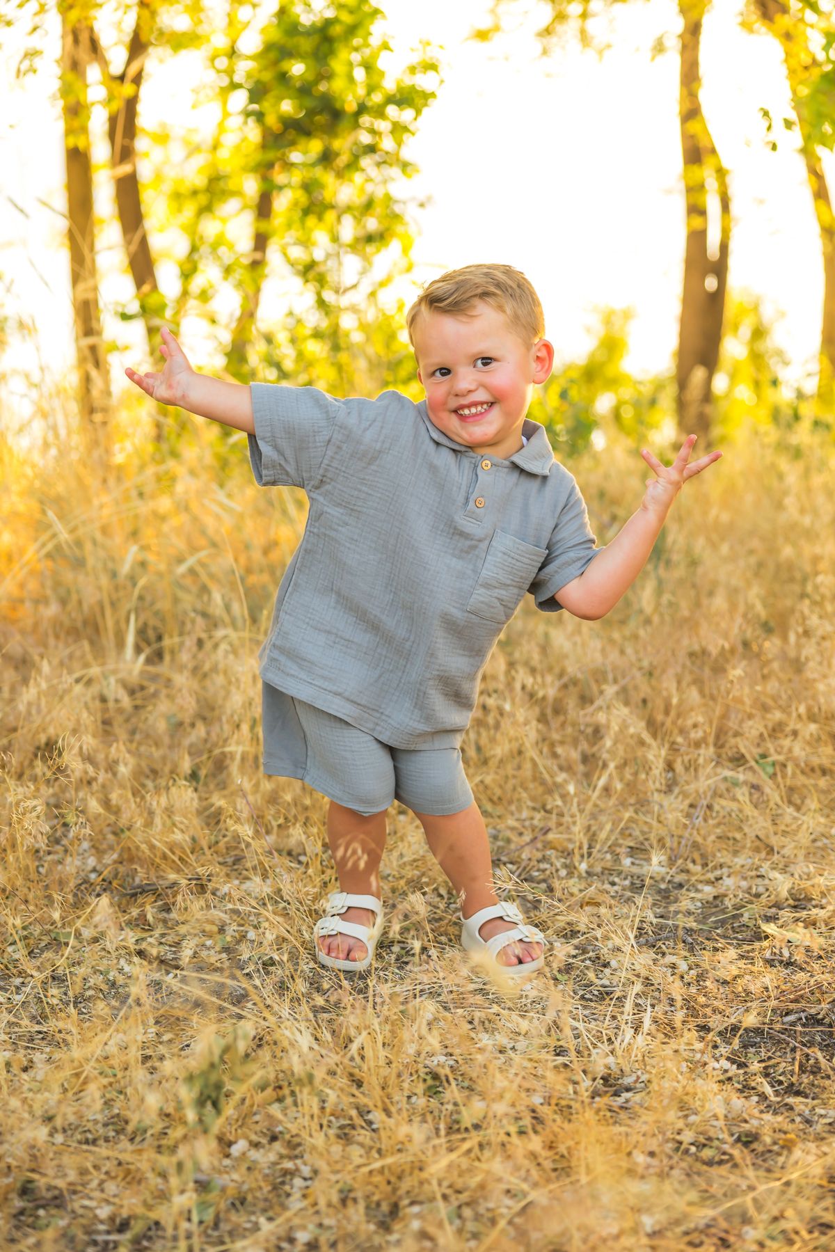 Child in gray outfit playing and making silly poses in golden sunlight.