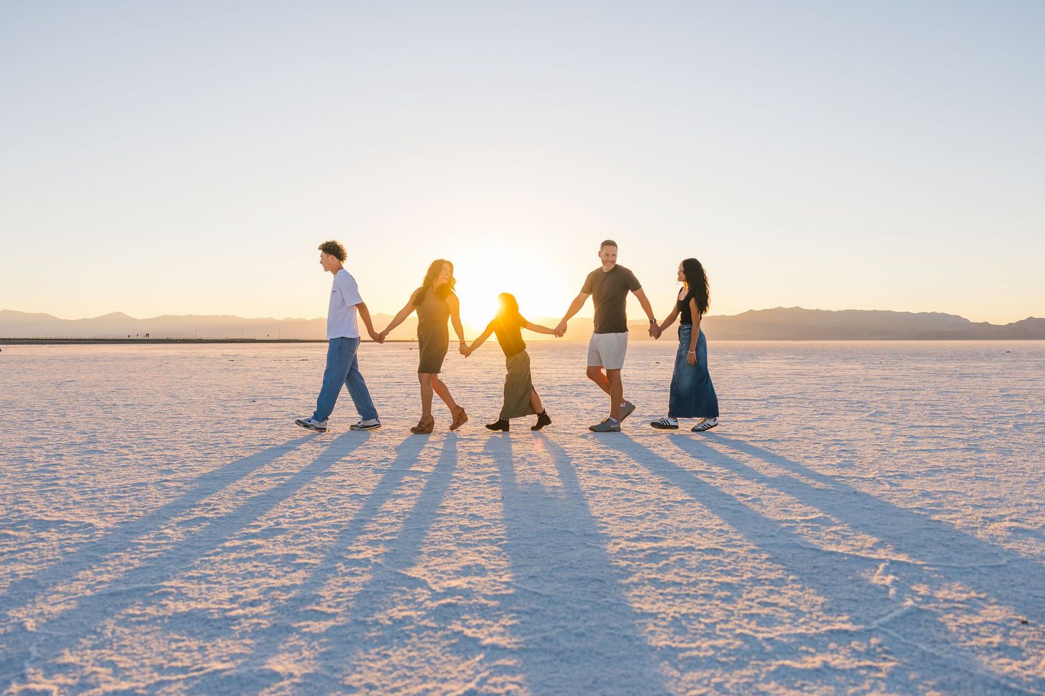 Group of people holding hands and walking across a pristine salt flat at sunset casting long shadows.