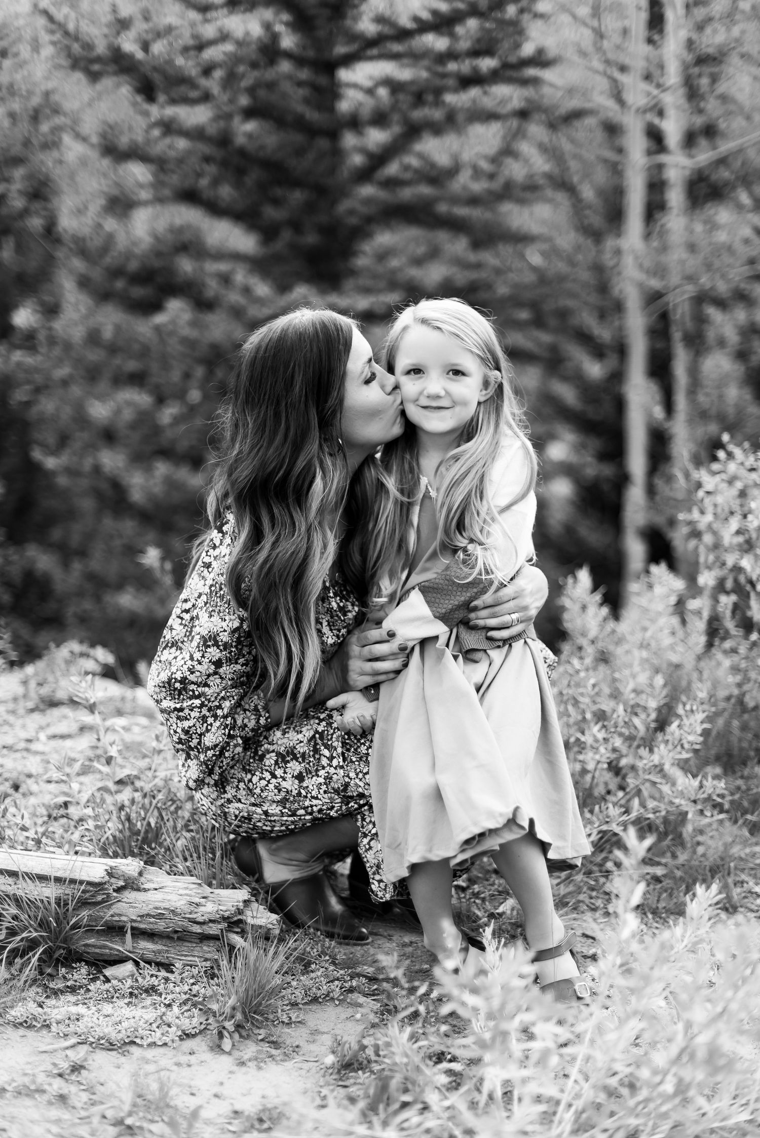 Two people sharing a tender moment outdoors in black and white photography with trees in the background.