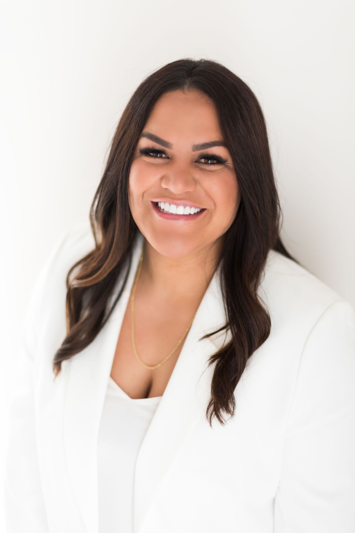 Professional headshot of a person in white blazer against light background.