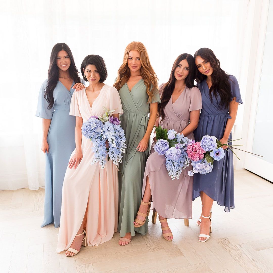Bridesmaids in pastel dresses hold hydrangea bouquets while posing against a white backdrop.