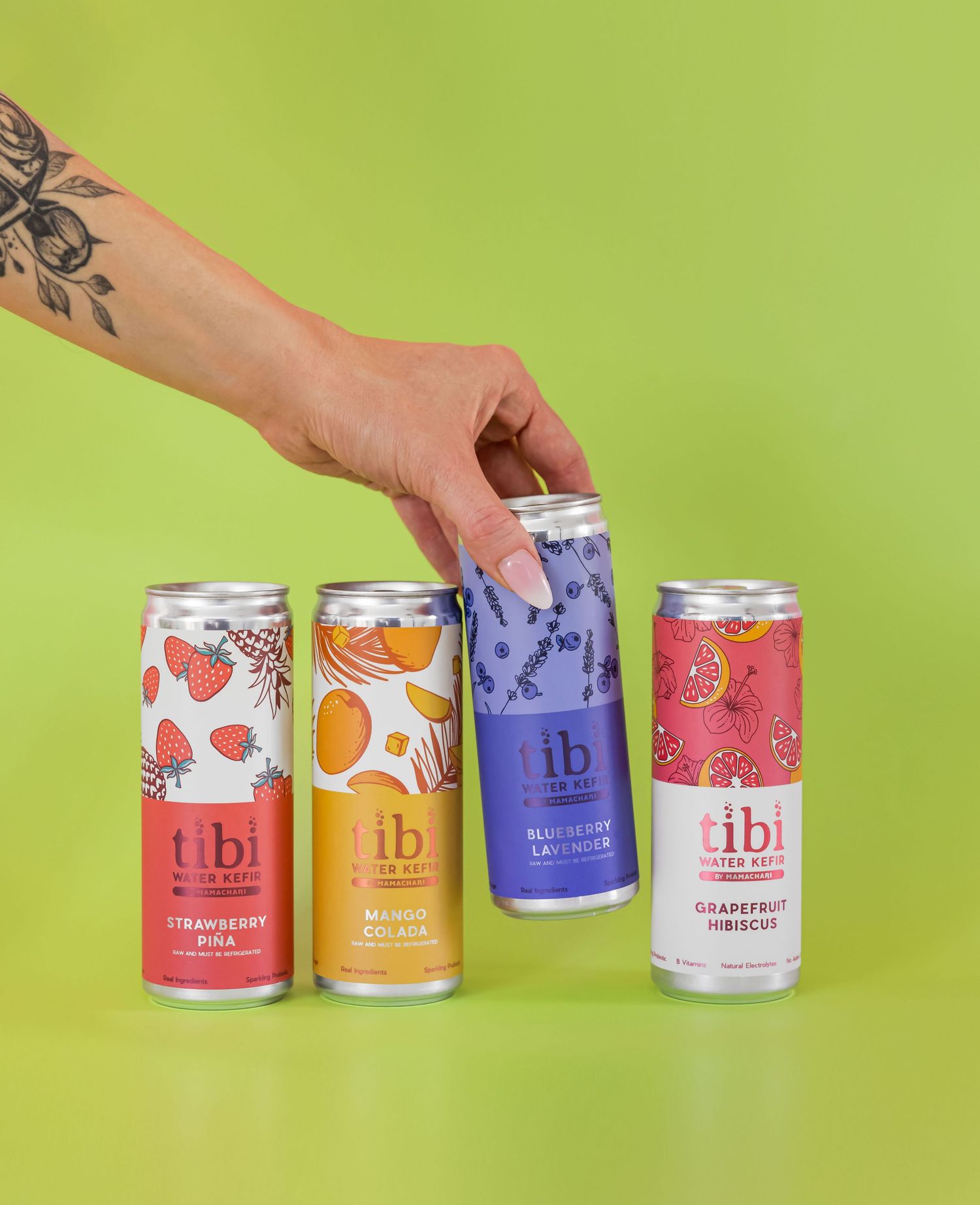 Tattooed hand reaching for colorful canned beverages against green background.