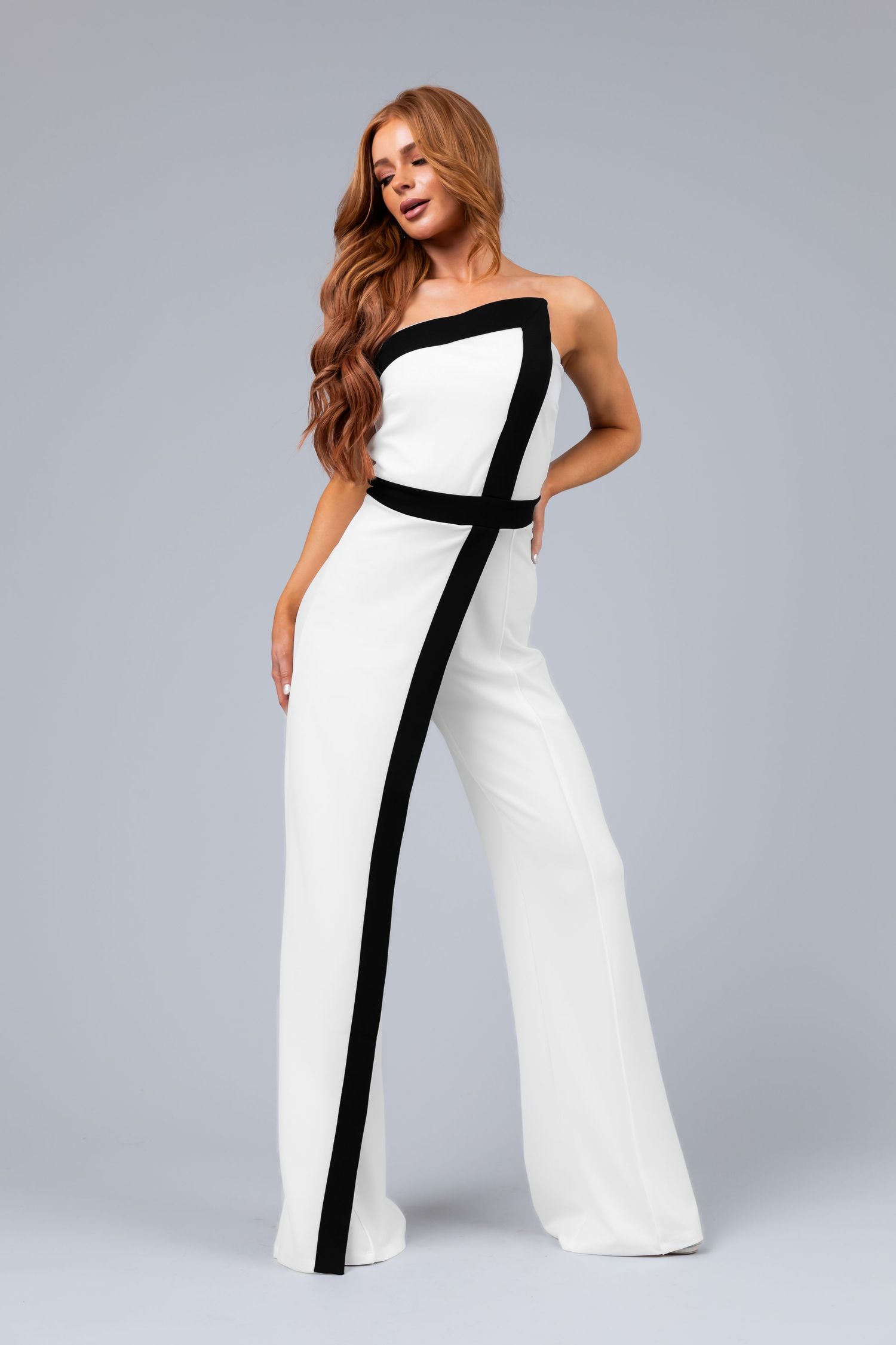 A model showcases a white strapless dress with a bold black vertical stripe detail in a studio photoshoot series.