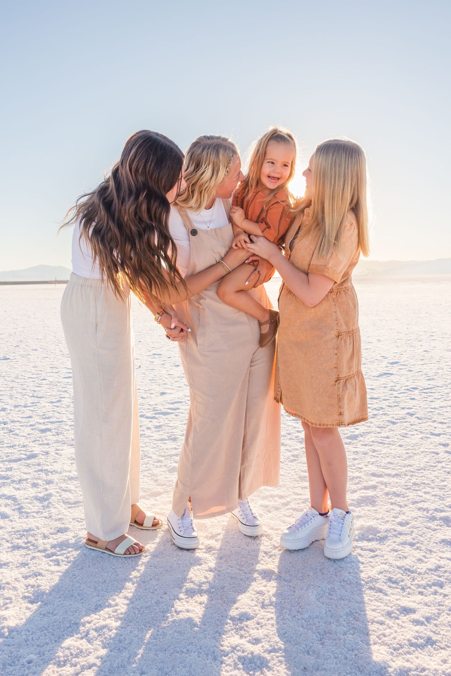 Group wearing neutral outfits laughing together on bright white snowy landscape.