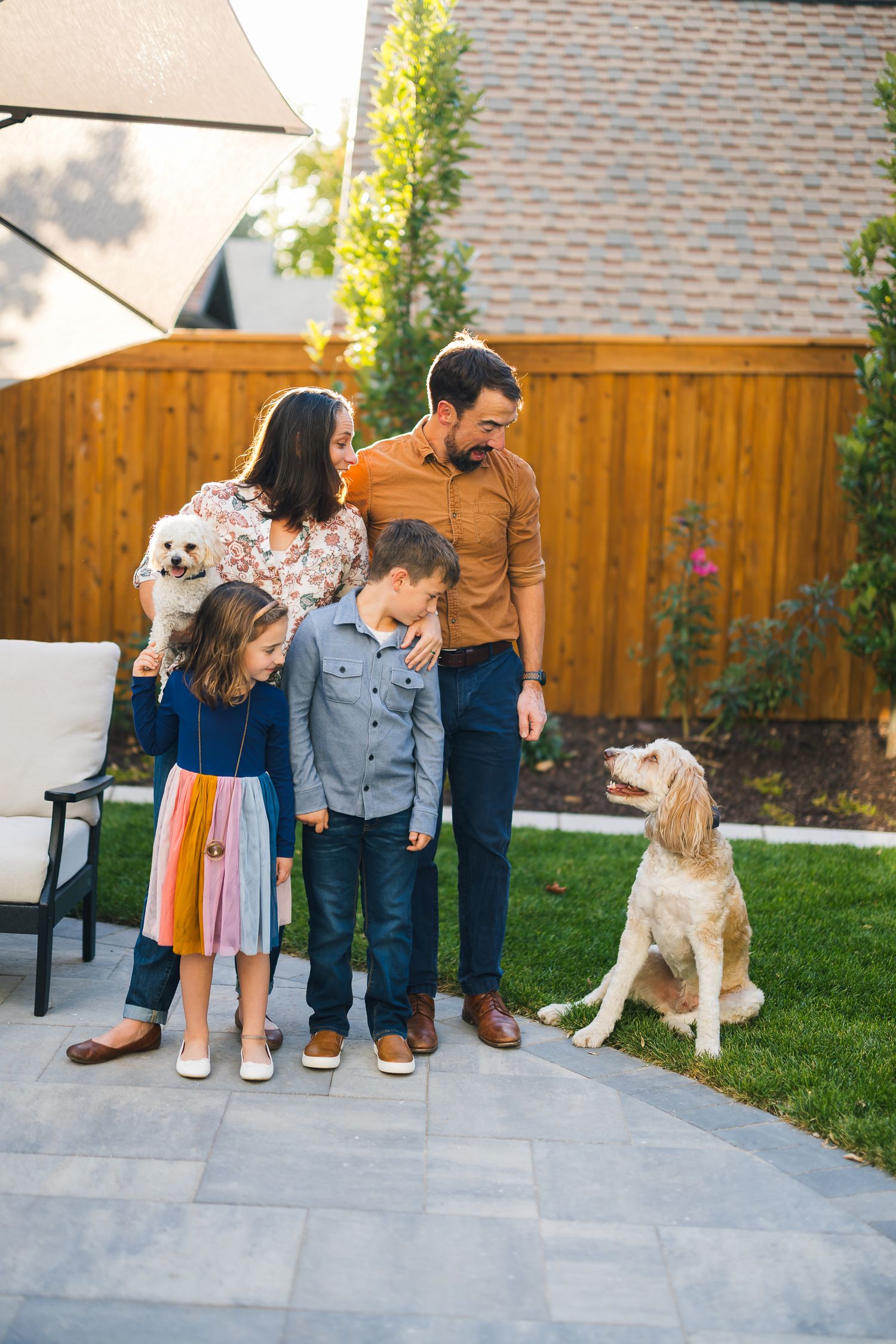 Family and their golden retriever dog pose together on stone patio under shade sail.