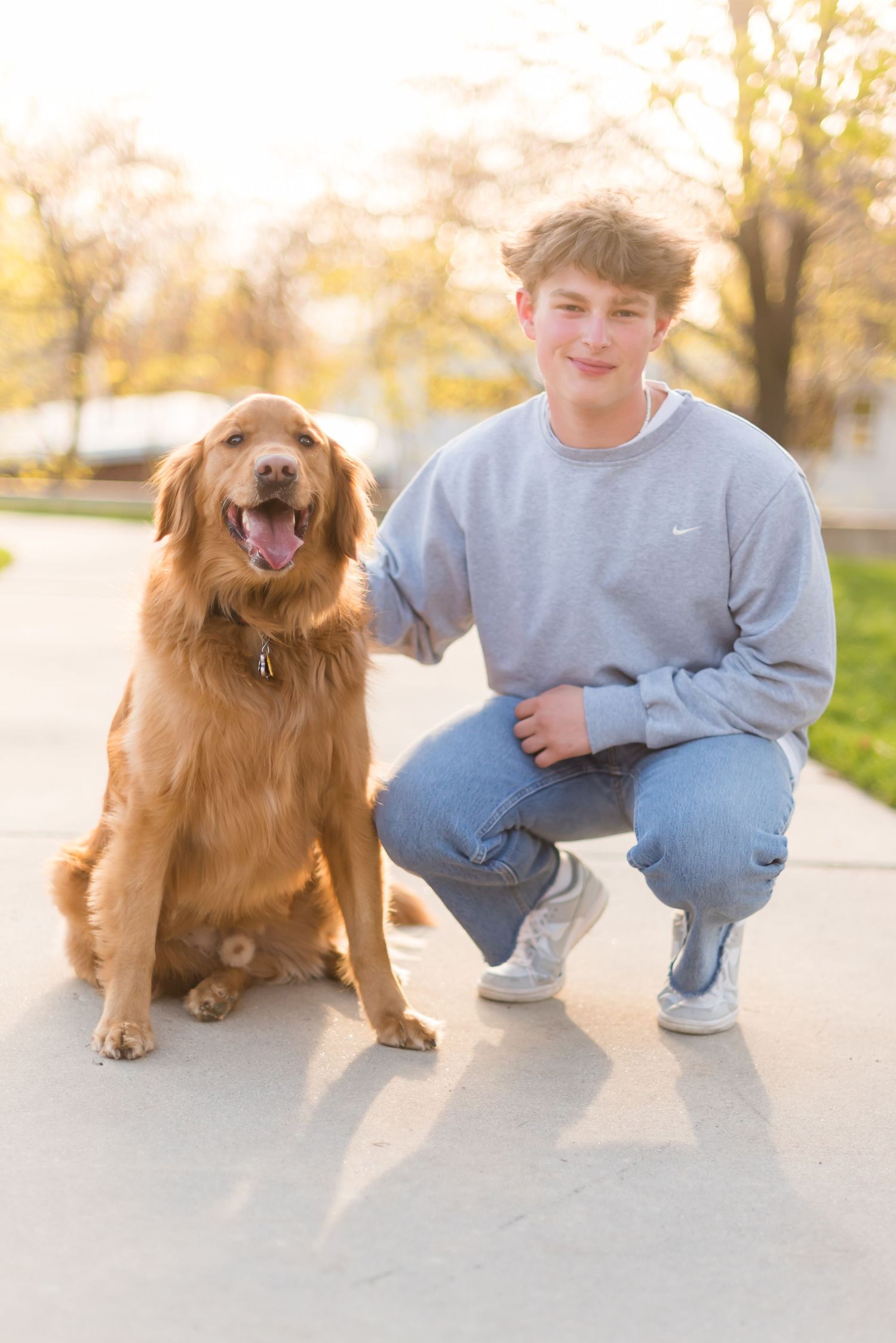 A Golden Retriever sits beside someone wearing a gray sweatshirt and jeans outdoors during golden hour.
