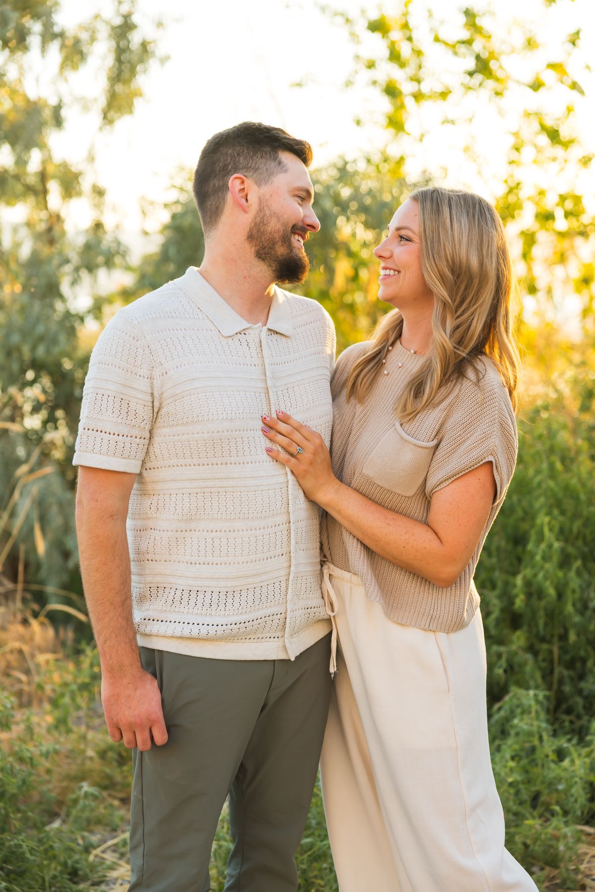 Couple in neutral-colored outfits sharing a joyful moment together in golden sunset light.