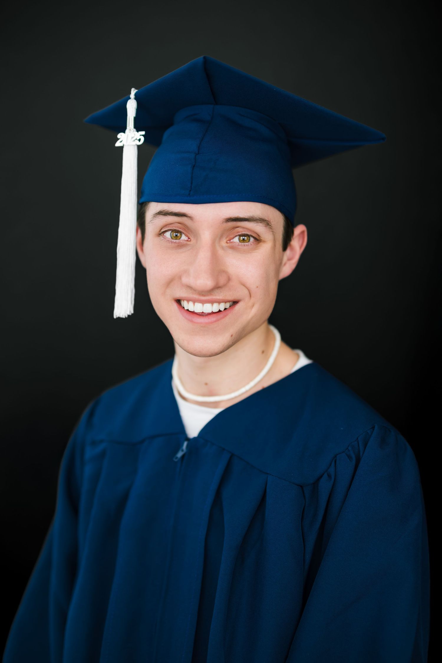 Graduation portraits of senior boy in salt lake city in navy blue cap and gown against dark background in modern studio
