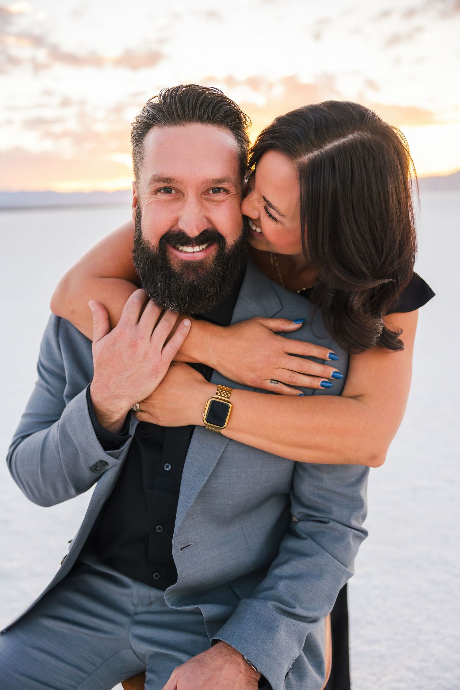 Couple sharing intimate moments in formal wear against sunset backdrop.