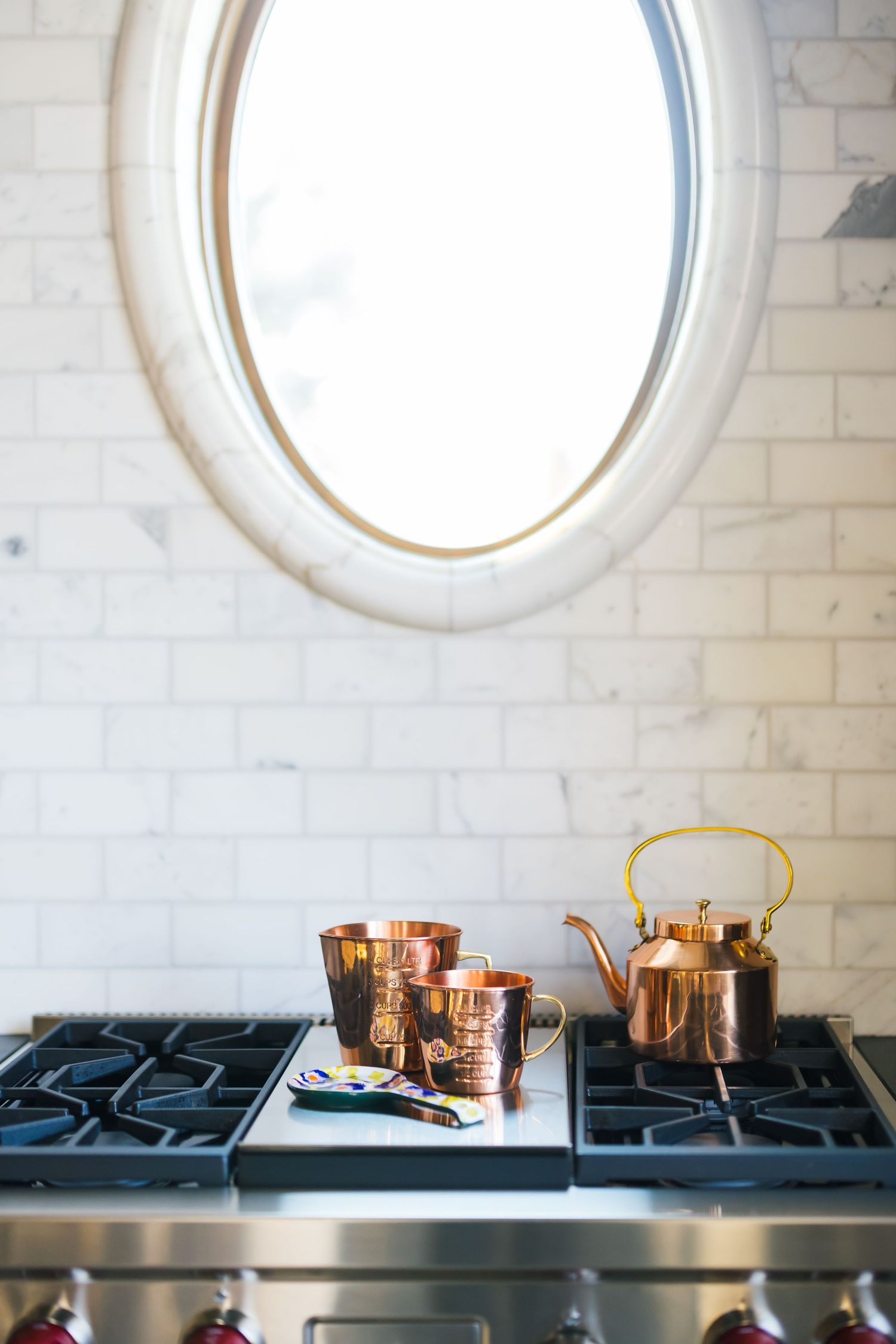 Copper cookware collection displayed beneath circular mirrors on white brick wall above black stovetop.