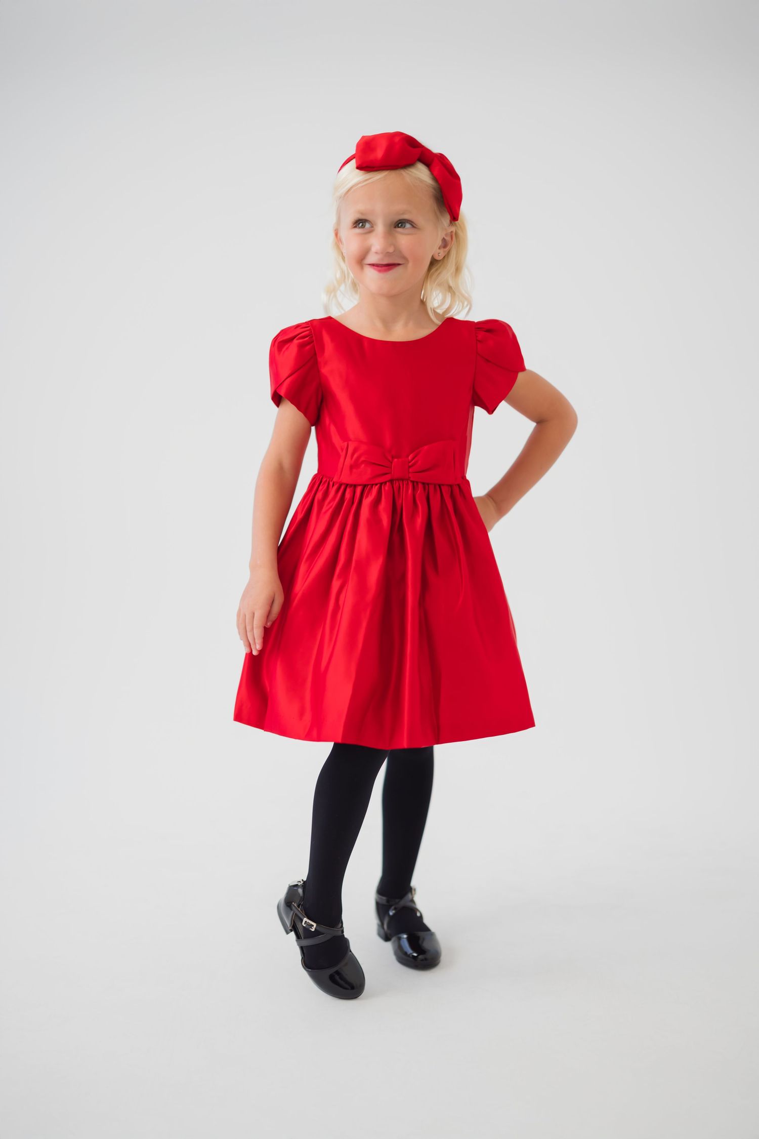 A child wearing a bright red dress with ruffled sleeves and black shoes poses against a white background in four views.