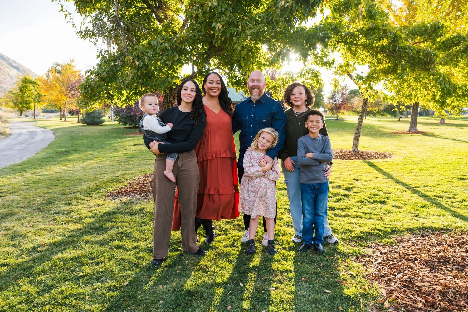 Family photo session in park during golden hour with natural sunlight filtering through trees in sandy, utah