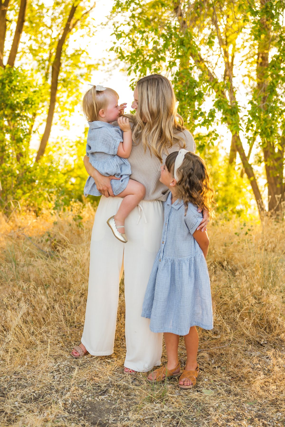 Family members embrace while wearing coordinated outfits in sunlit outdoor setting.