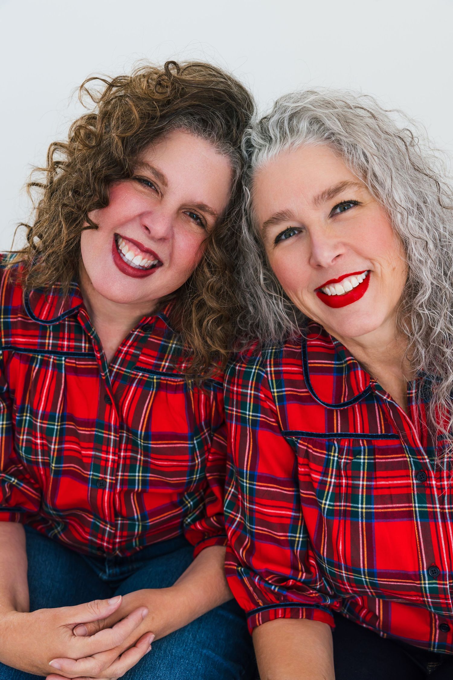 Two people wearing matching red plaid shirts share bright smiles while sitting together.