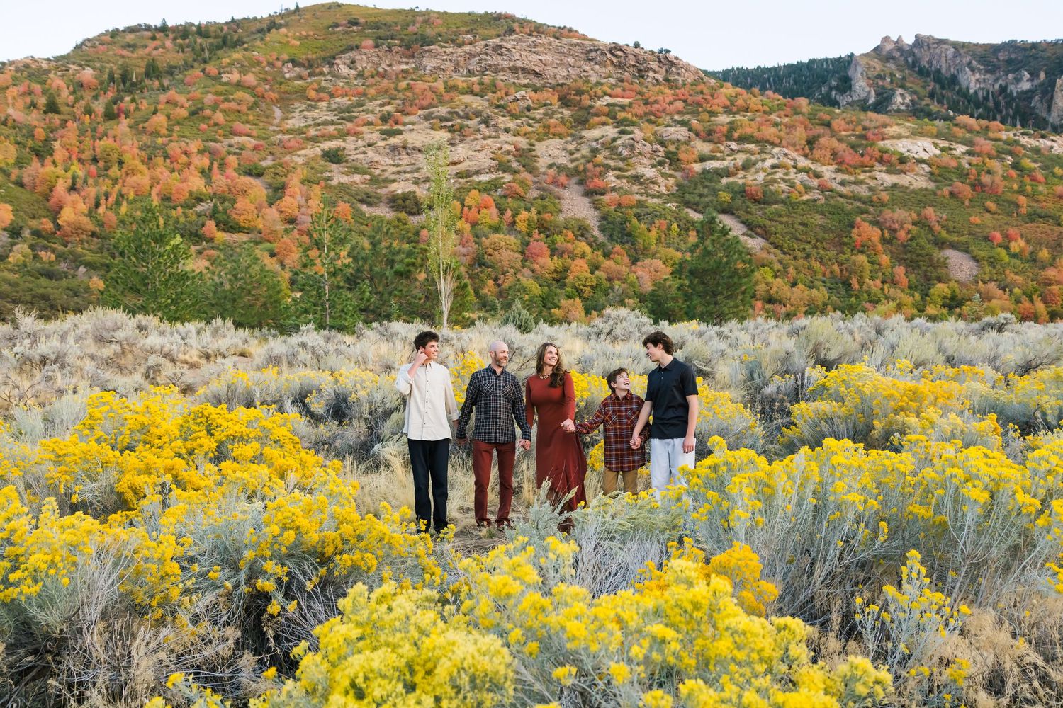 Group hiking through yellow wildflowers and sagebrush with autumn-colored mountains in the background.