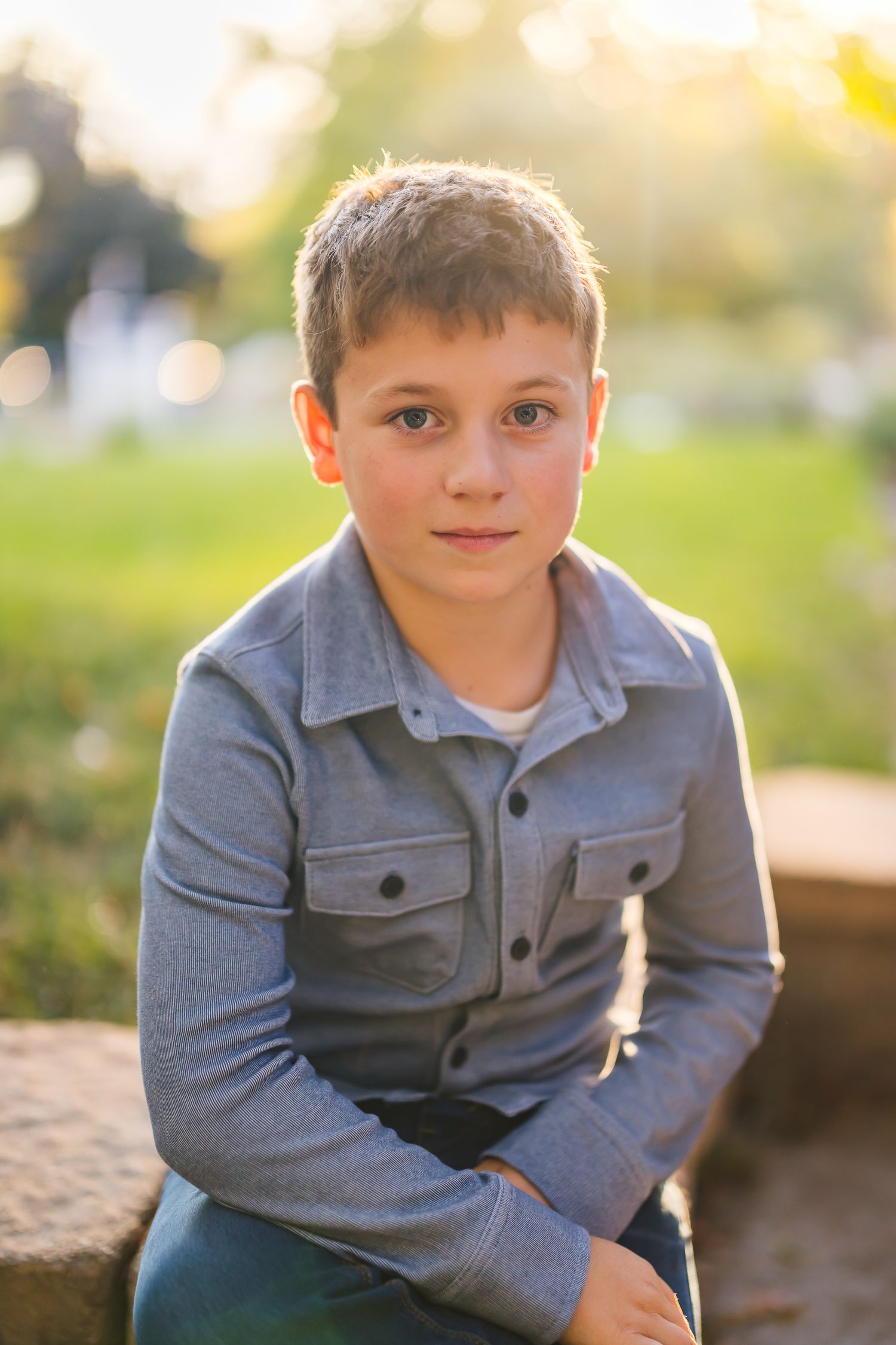 Portrait of a young boy in a grey button-up shirt outdoors at sunset.