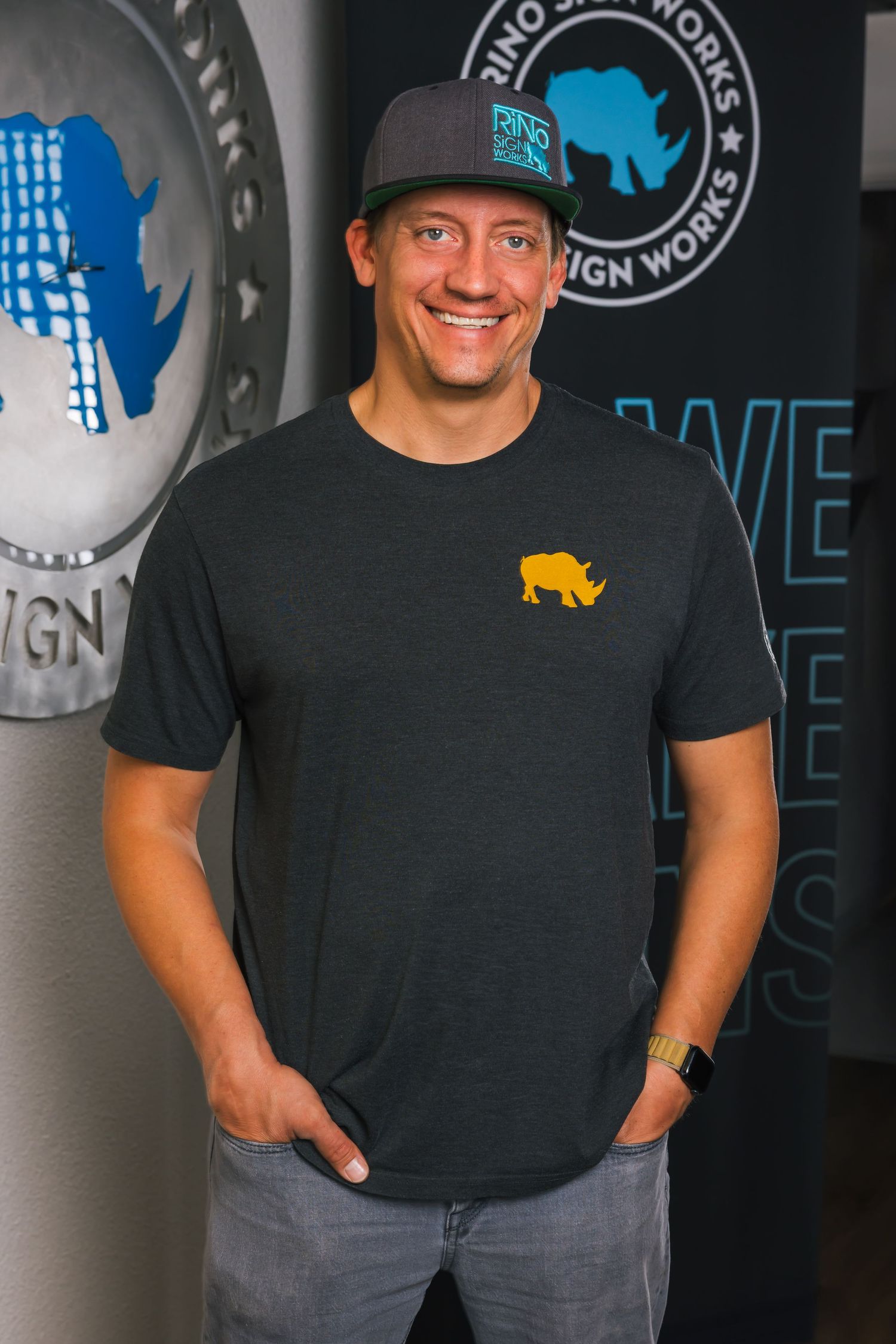 A person wearing a black t-shirt with a yellow buffalo logo and baseball cap stands against a wall with rhino designs.