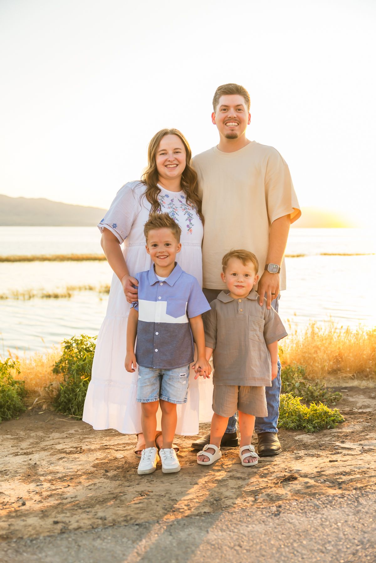 Family stands together on rocky path at sunset near waterfront.