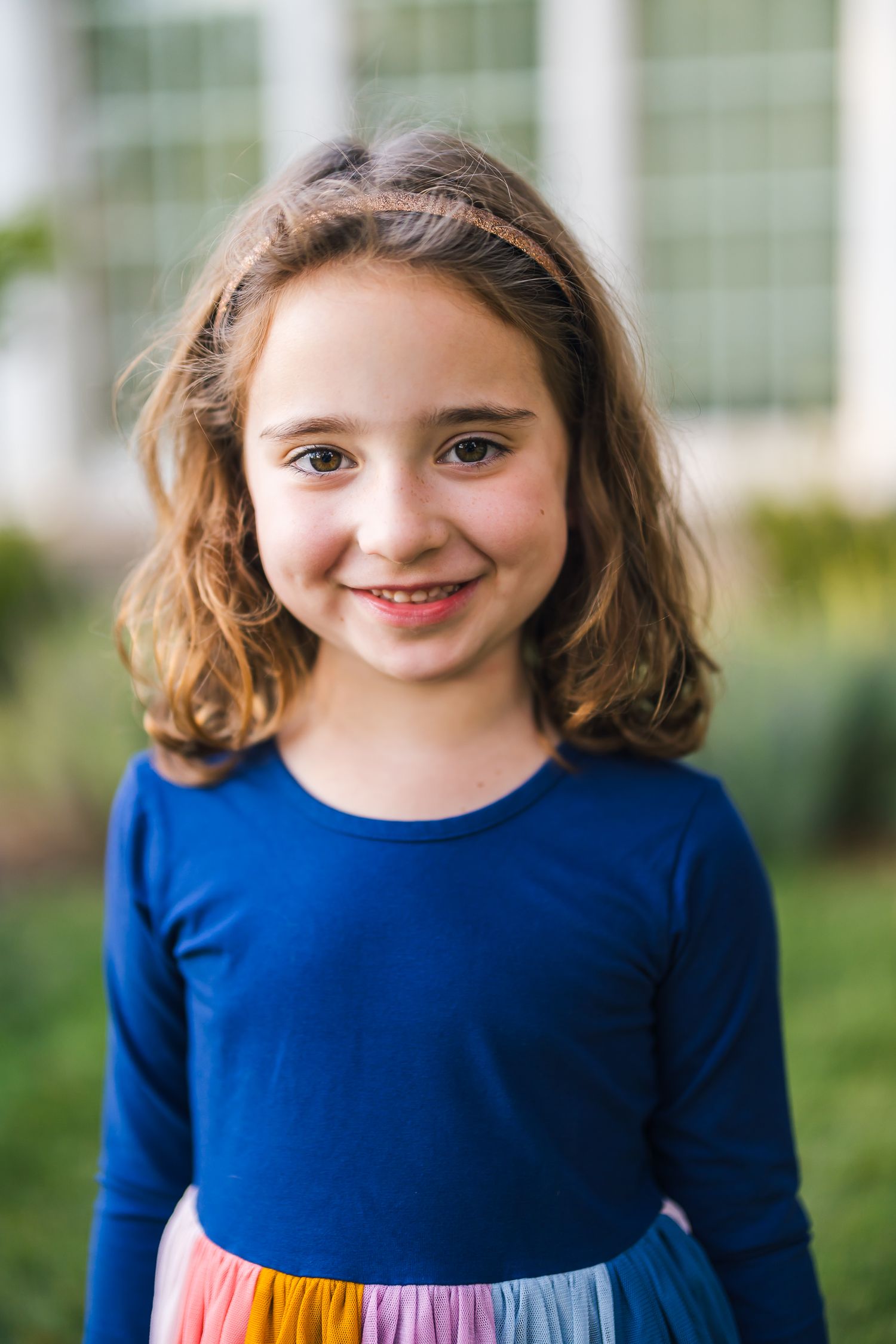 Young girl smiles while wearing a blue top with rainbow skirt.