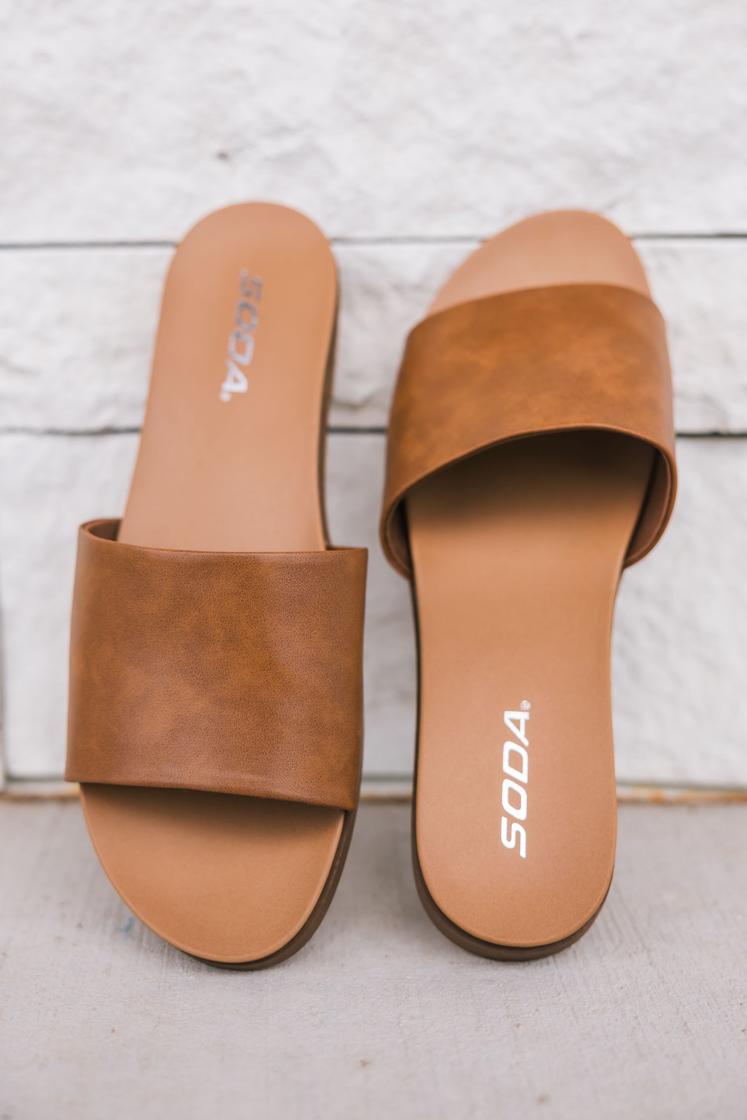 Tan leather slide sandals with a wide single strap and SODA branding on white wooden background.