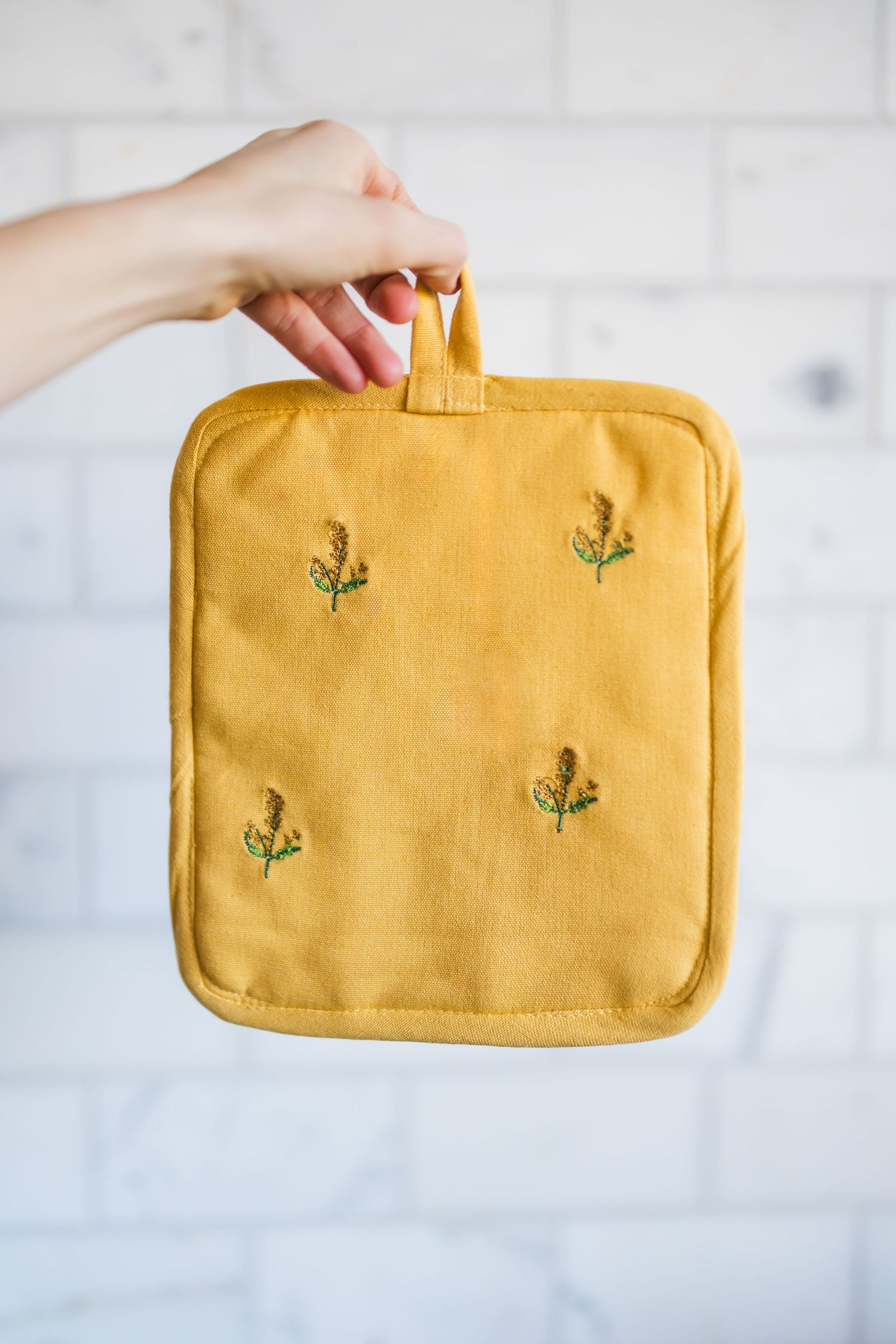 A mustard yellow linen makeup bag with small embroidered cactus designs displayed against a white background.