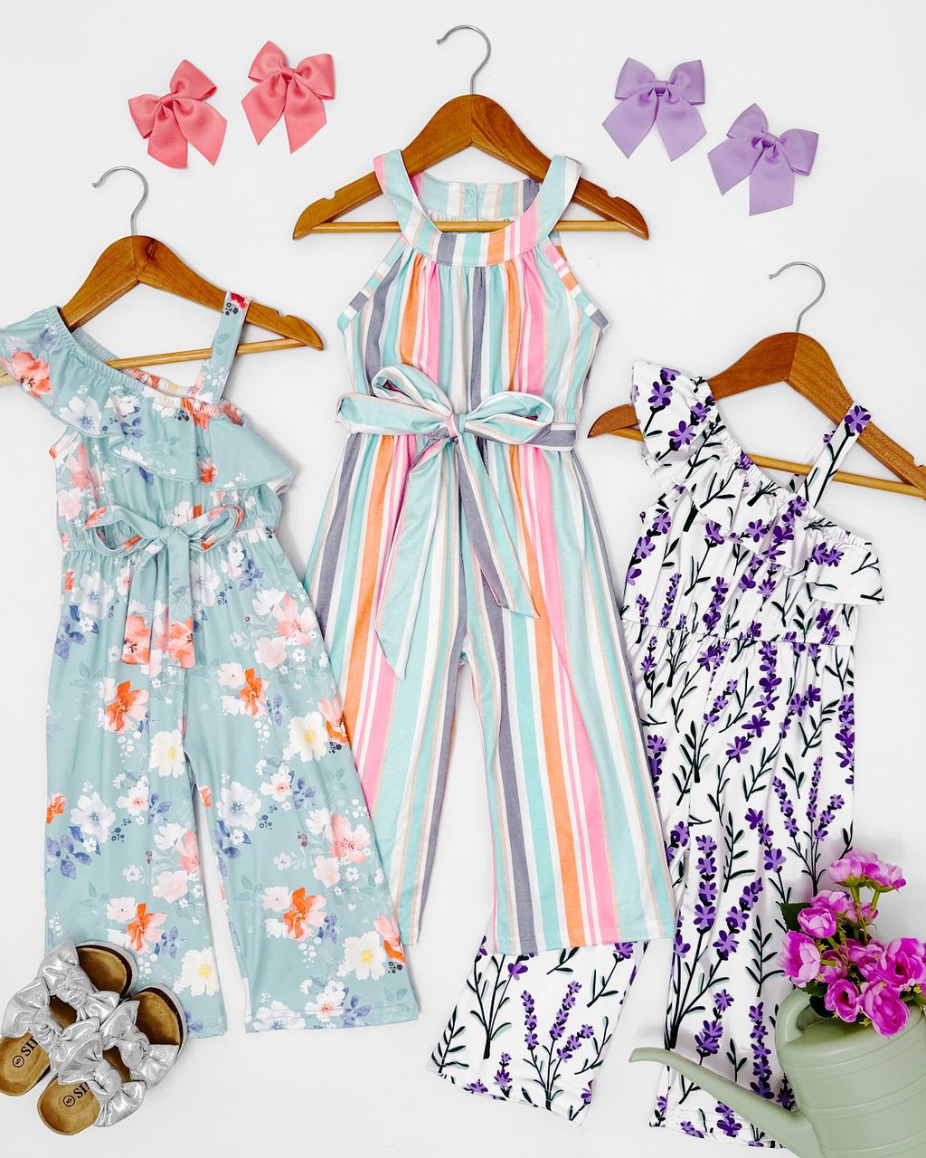A collection of pastel floral and striped baby girl dresses on wooden hangers displayed side by side.