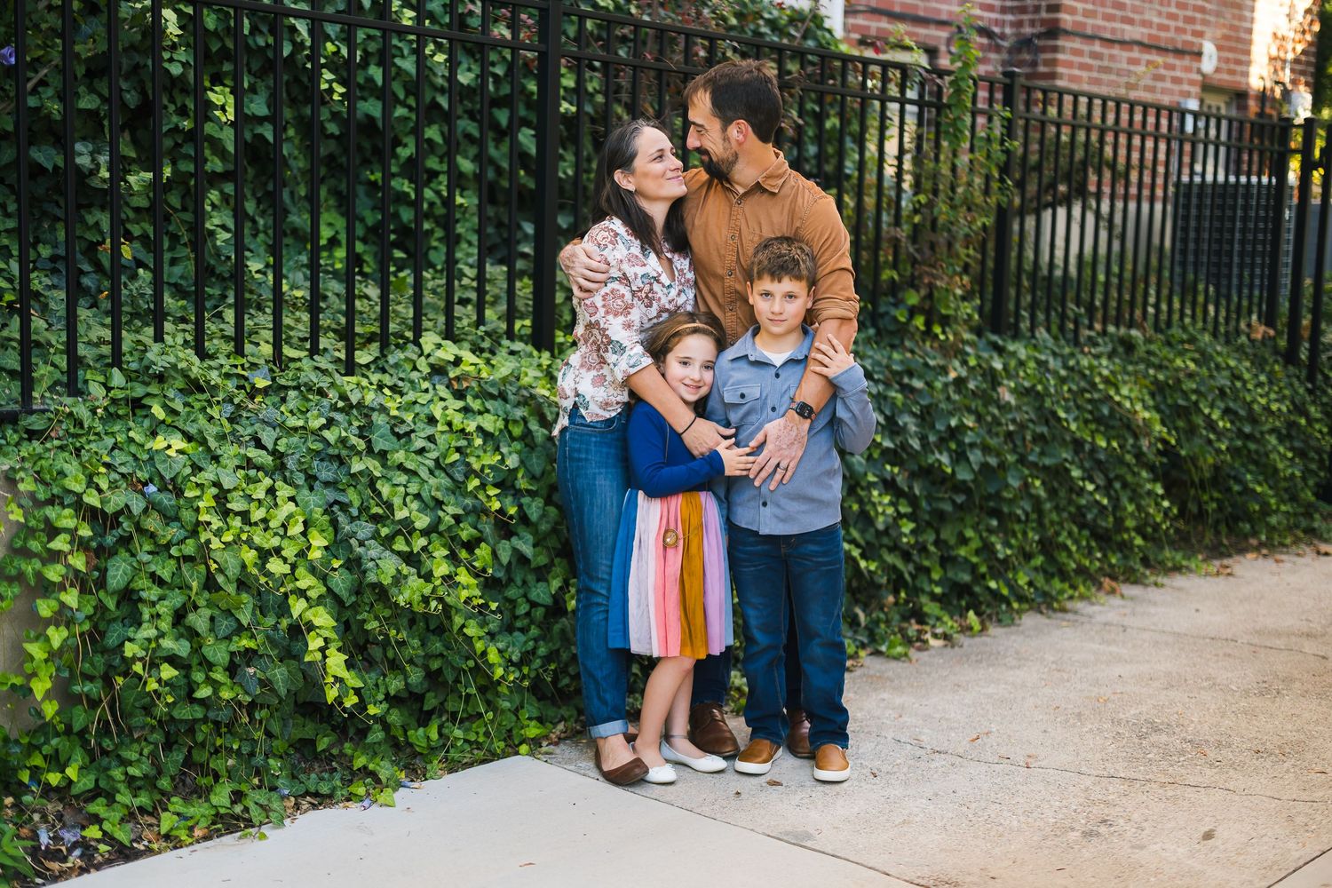 Casual family portrait against garden backdrop with iron fence and brick building.