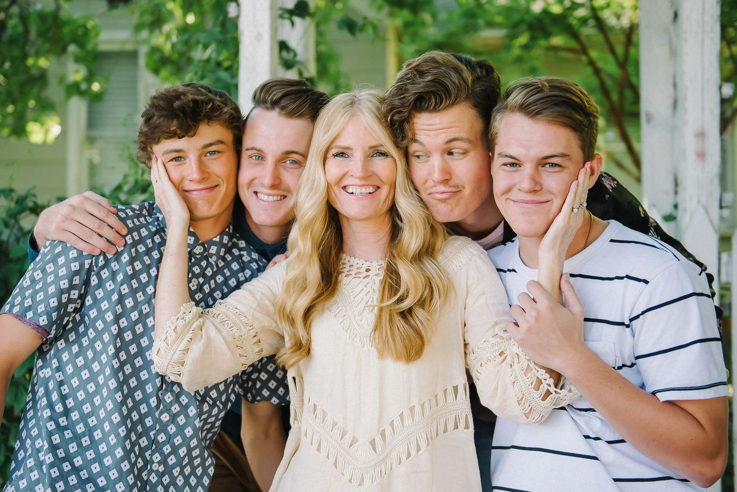A group of young friends pose together outdoors against a white porch backdrop.