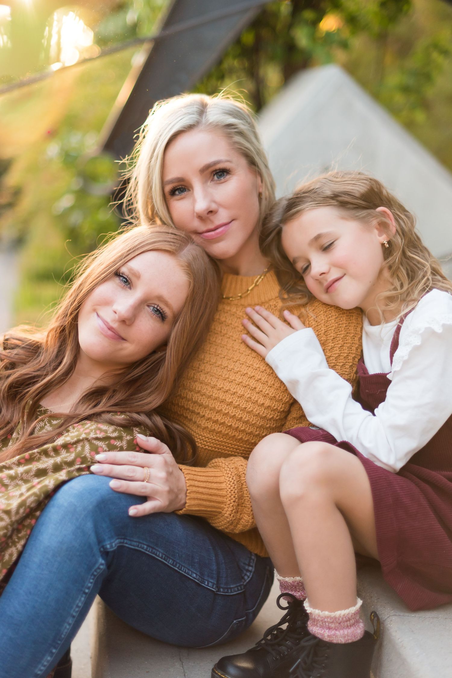 Three people in autumn sweaters and dresses share an intimate moment outdoors.