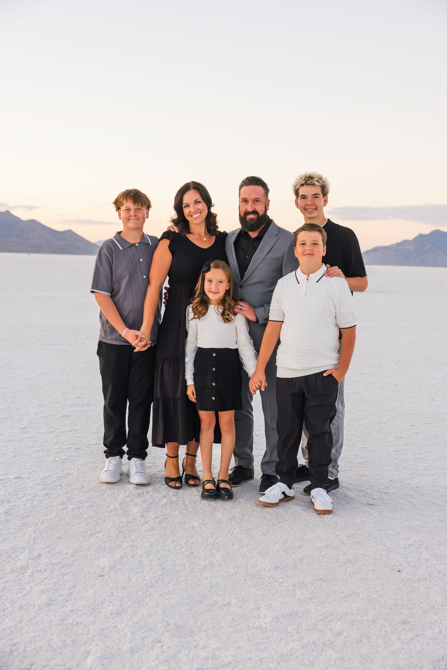 A family of five stands together on the white salt flats against a mountain backdrop at sunset.