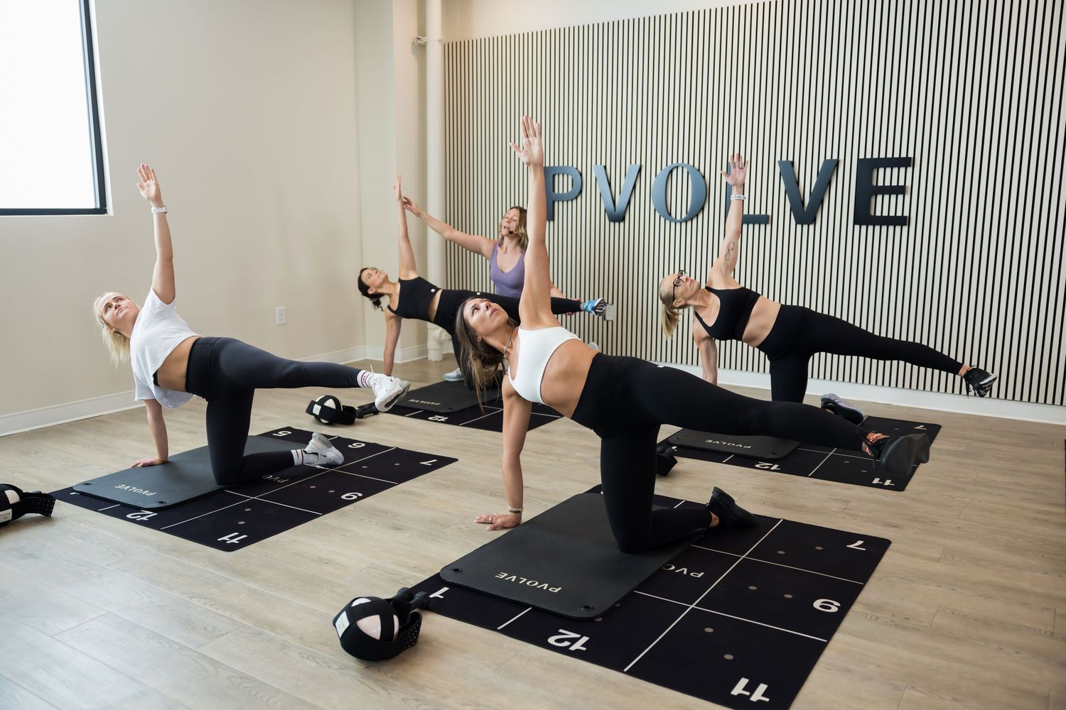Person practicing various yoga poses and stretches on black exercise mats in a modern studio with striped wall.
