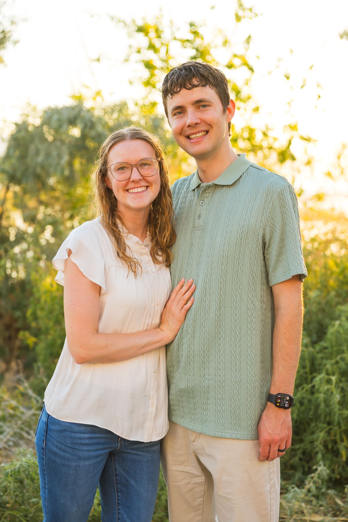 Couple in casual attire poses together outdoors during golden hour photo session.