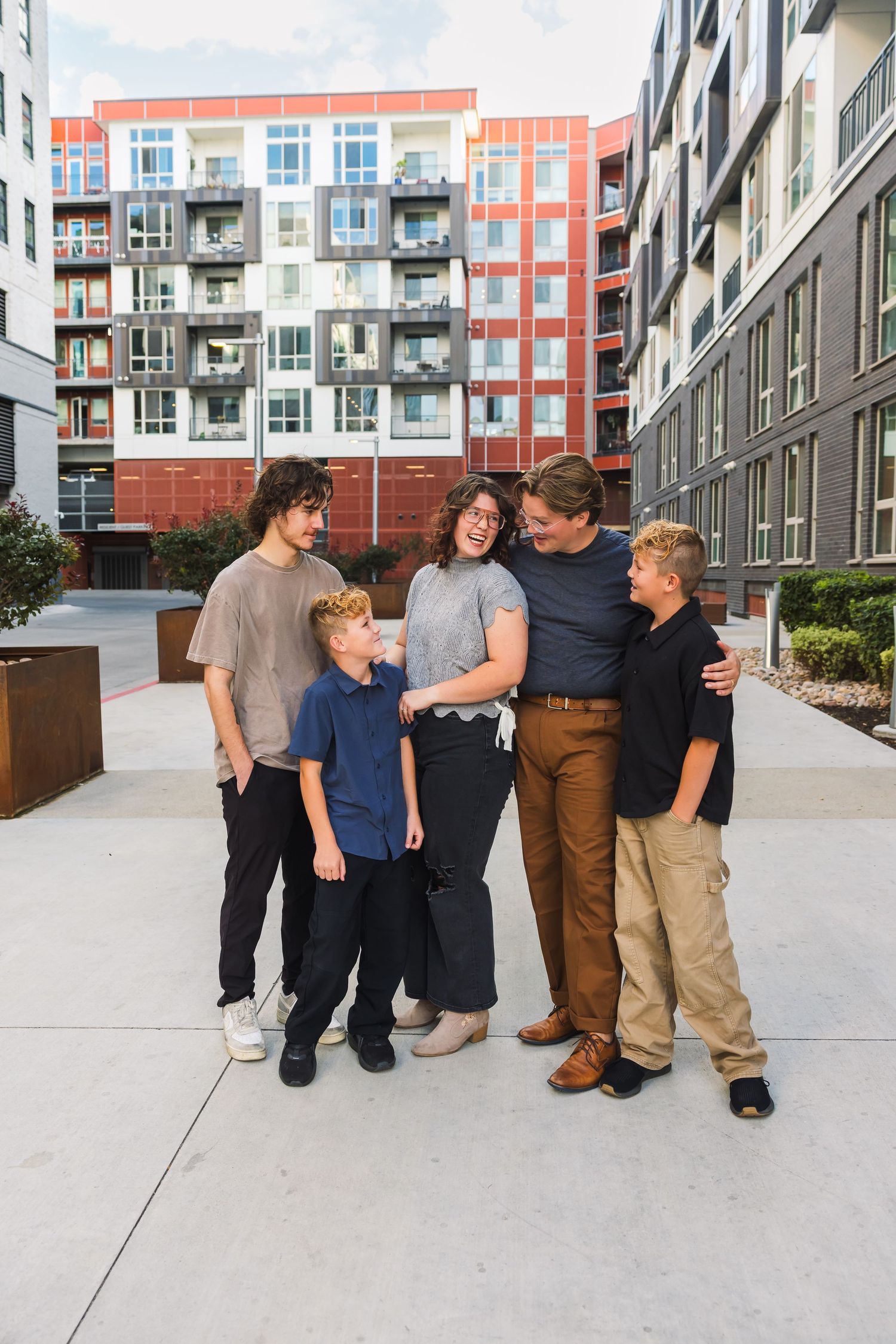 Group of friends laughing and interacting together in front of modern apartment building courtyard.